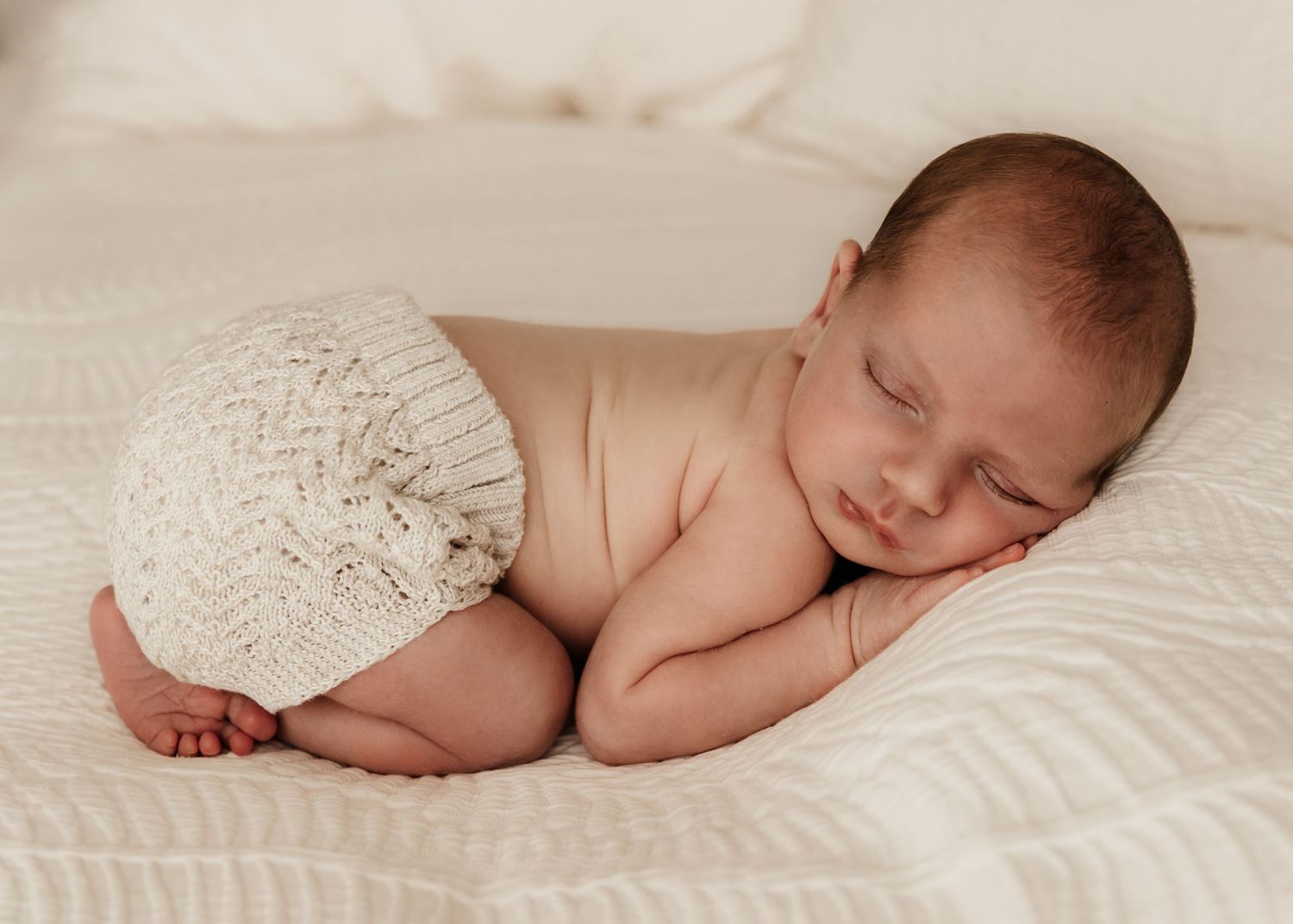Newborn baby asleep in bum-up pose in just a nappy on parent's bed during an at-home newborn photoshoot in Dubai