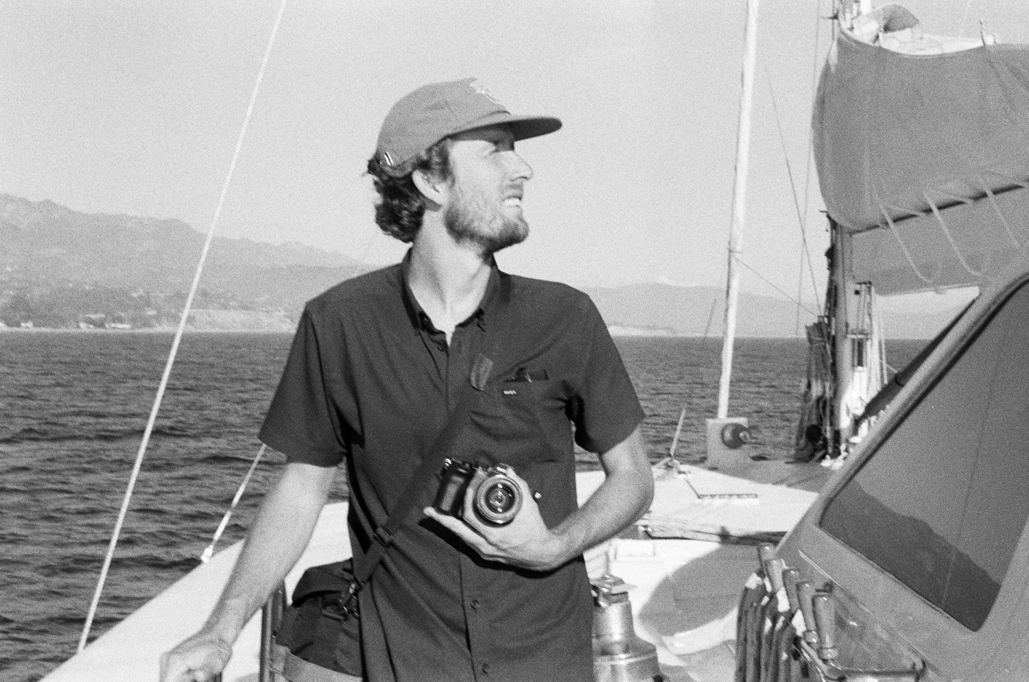 Black and white photo of person with camera on sailboat looking at ocean view.