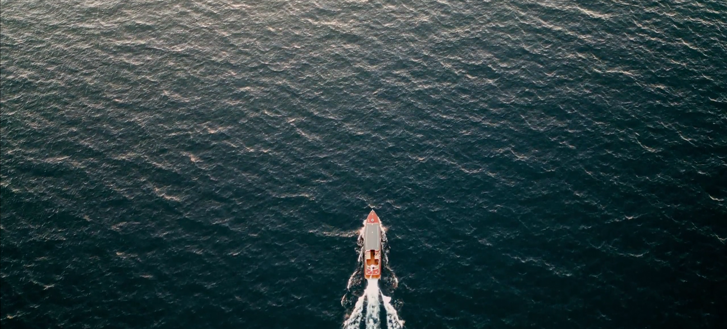 Aerial view of a small boat moving across dark rippling ocean waters.