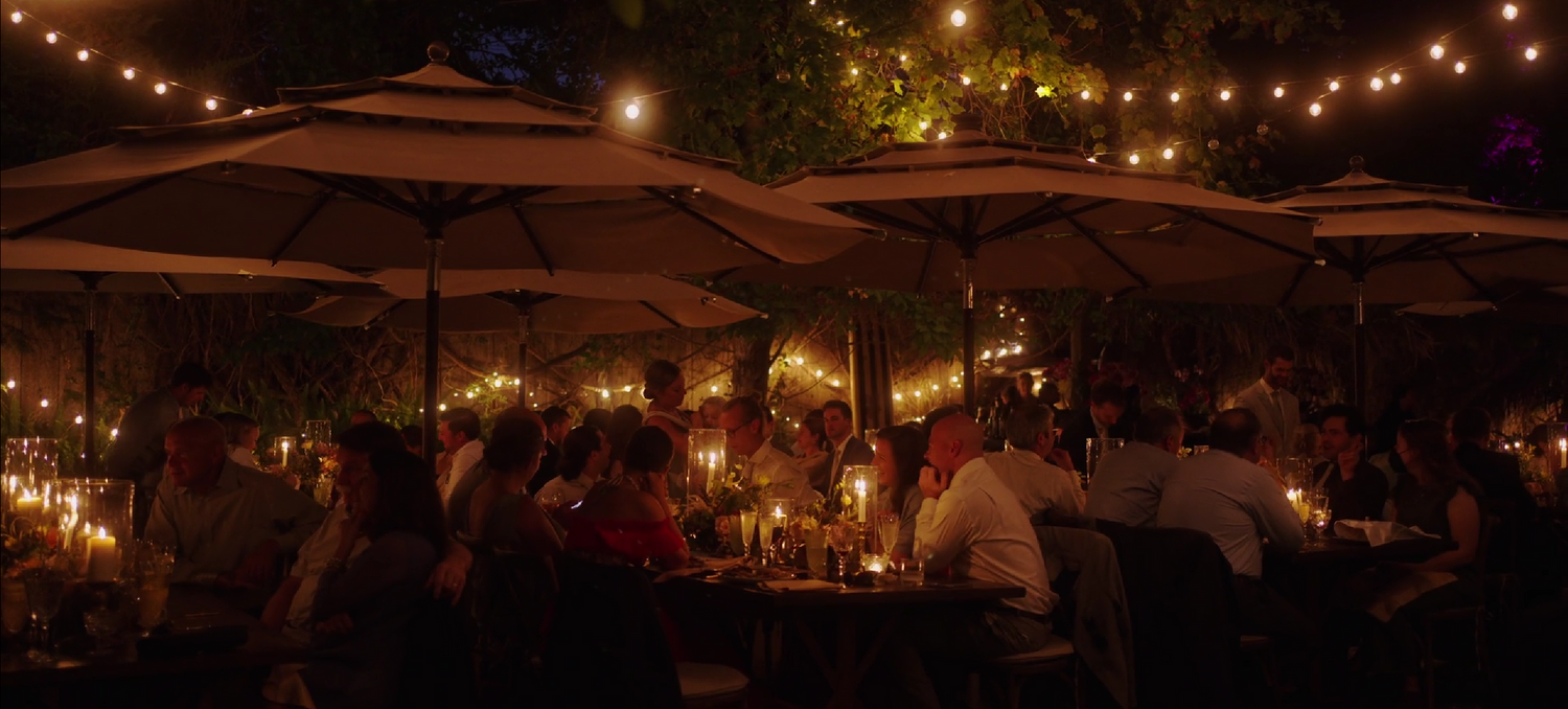 String lights illuminate umbrellas and tables at an outdoor evening dining setting.