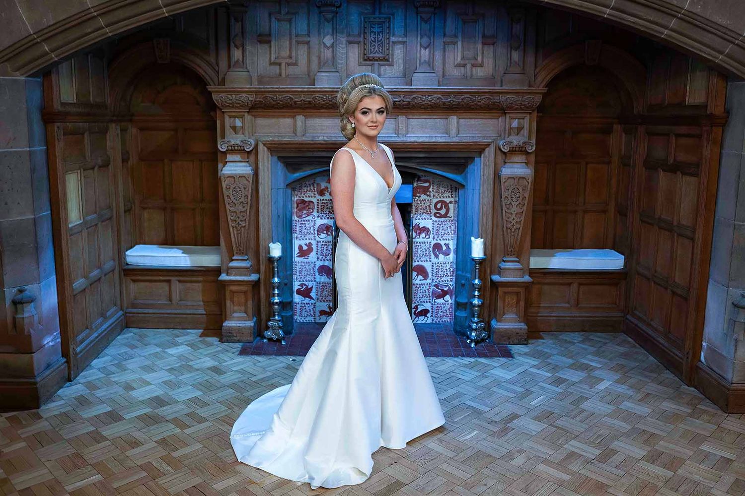 Bride in white mermaid wedding gown standing in elegant wood-paneled room with ornate fireplace at Dalston hall cumbria