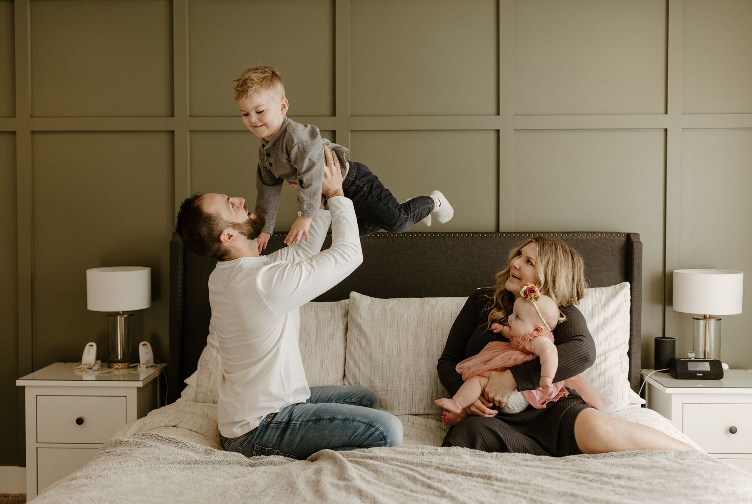 A mother is embracing her young son while sitting on a bed with another child in the background. Fort Worth Texas family photographer.