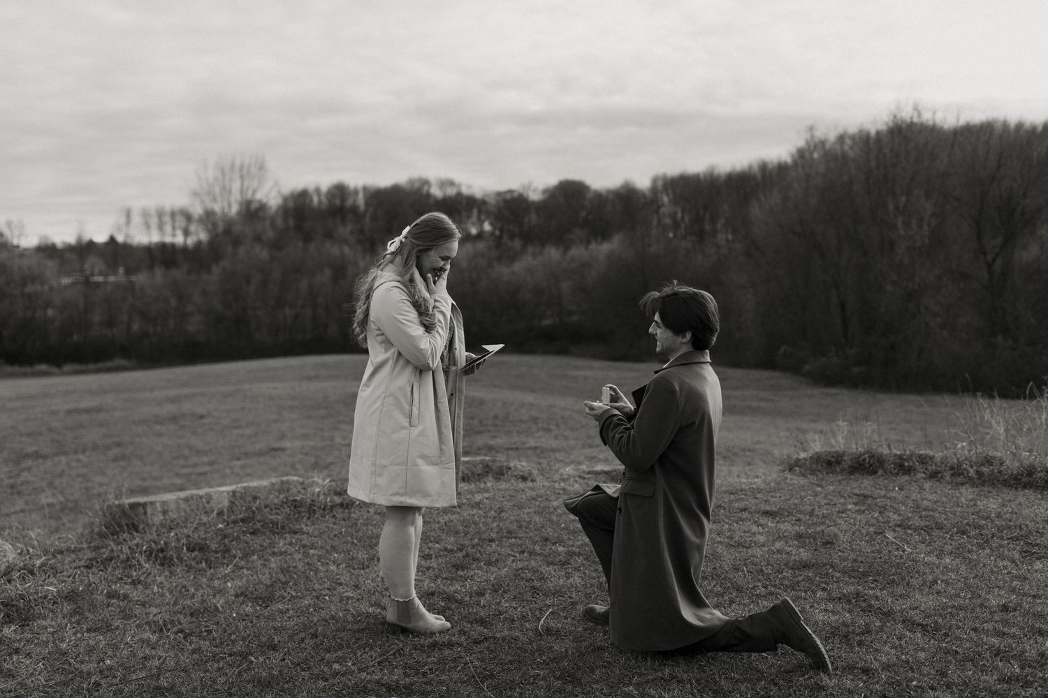 A black and white photograph shows a woman standing and a person kneeling in a field with trees in the background. Fort Worth Texas