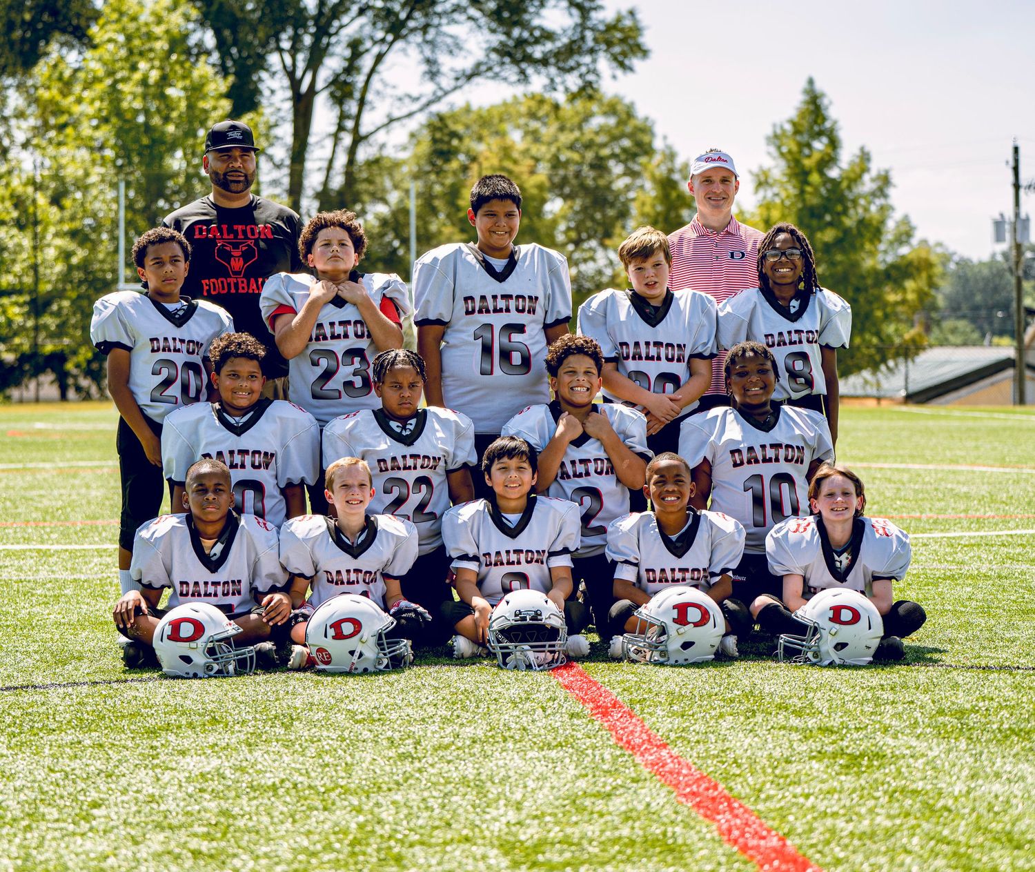 Youth football team poses for group photo on grass field with helmets.