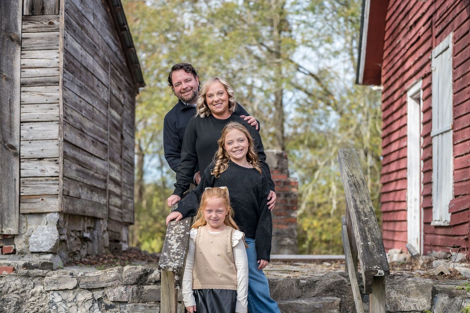 Family portraits by rustic stone wall and red barn exterior.