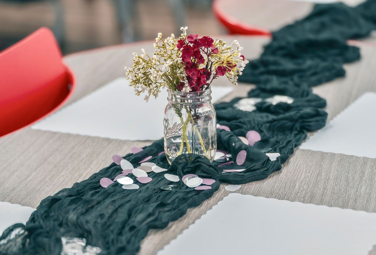 Table setting with black fabric runner and small floral centerpiece in glass vase.
