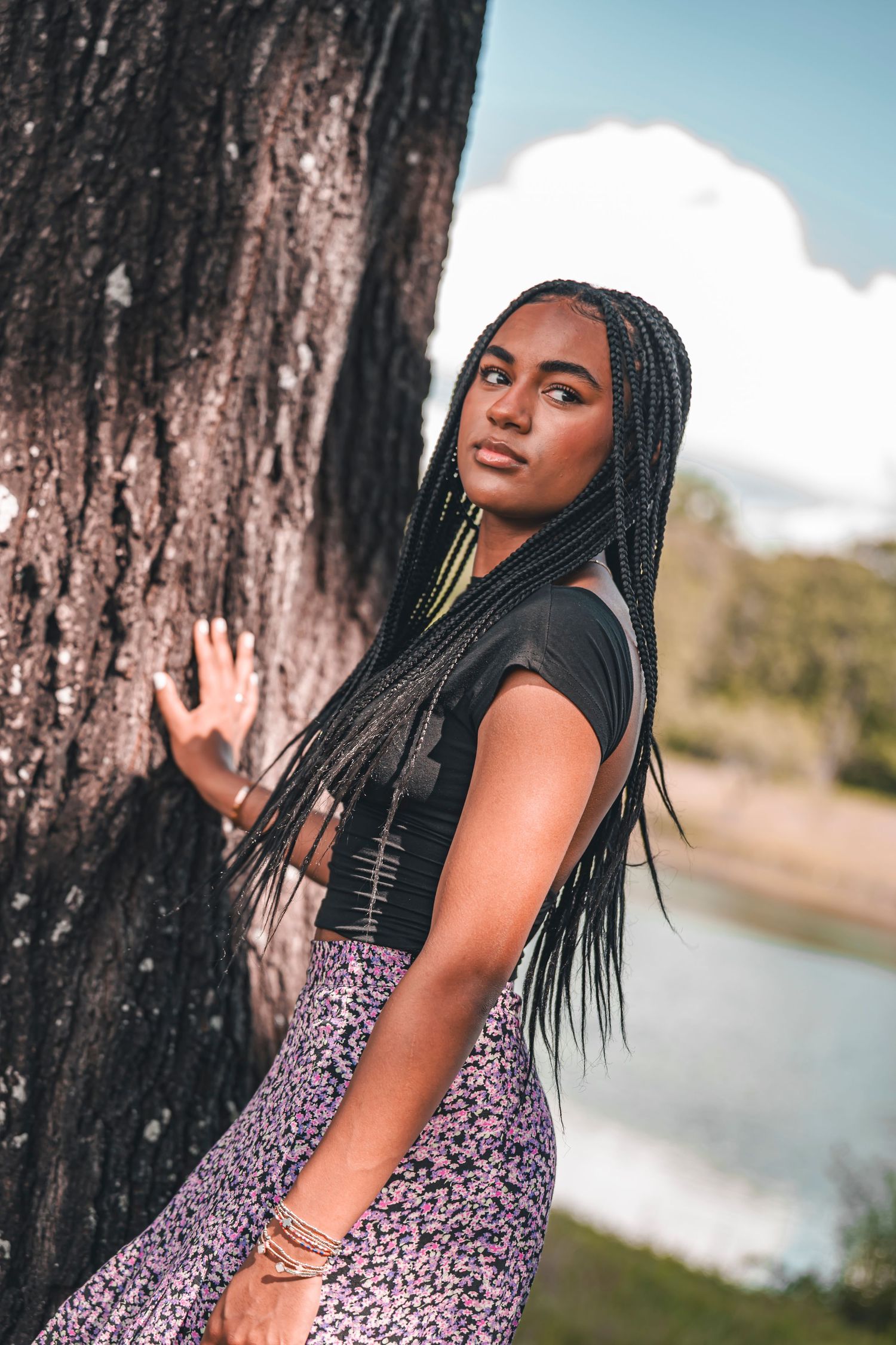 Artistic outdoor portrait session near a tree trunk by a lake on a sunny day.