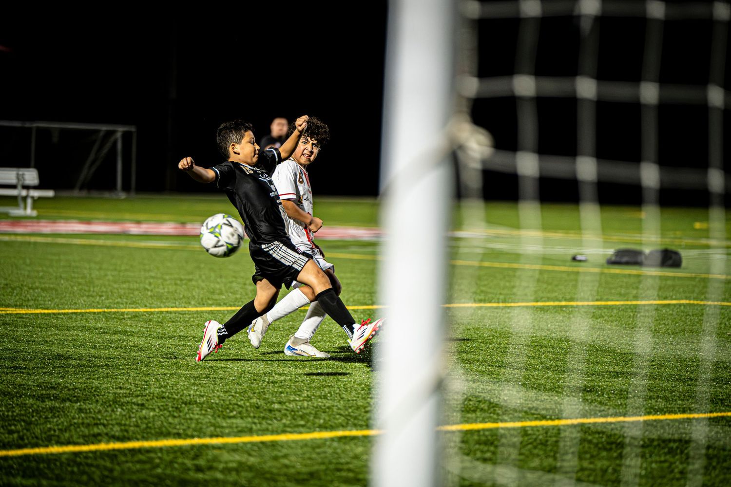 Soccer goal sequence showing match action through goal posts on evening field.