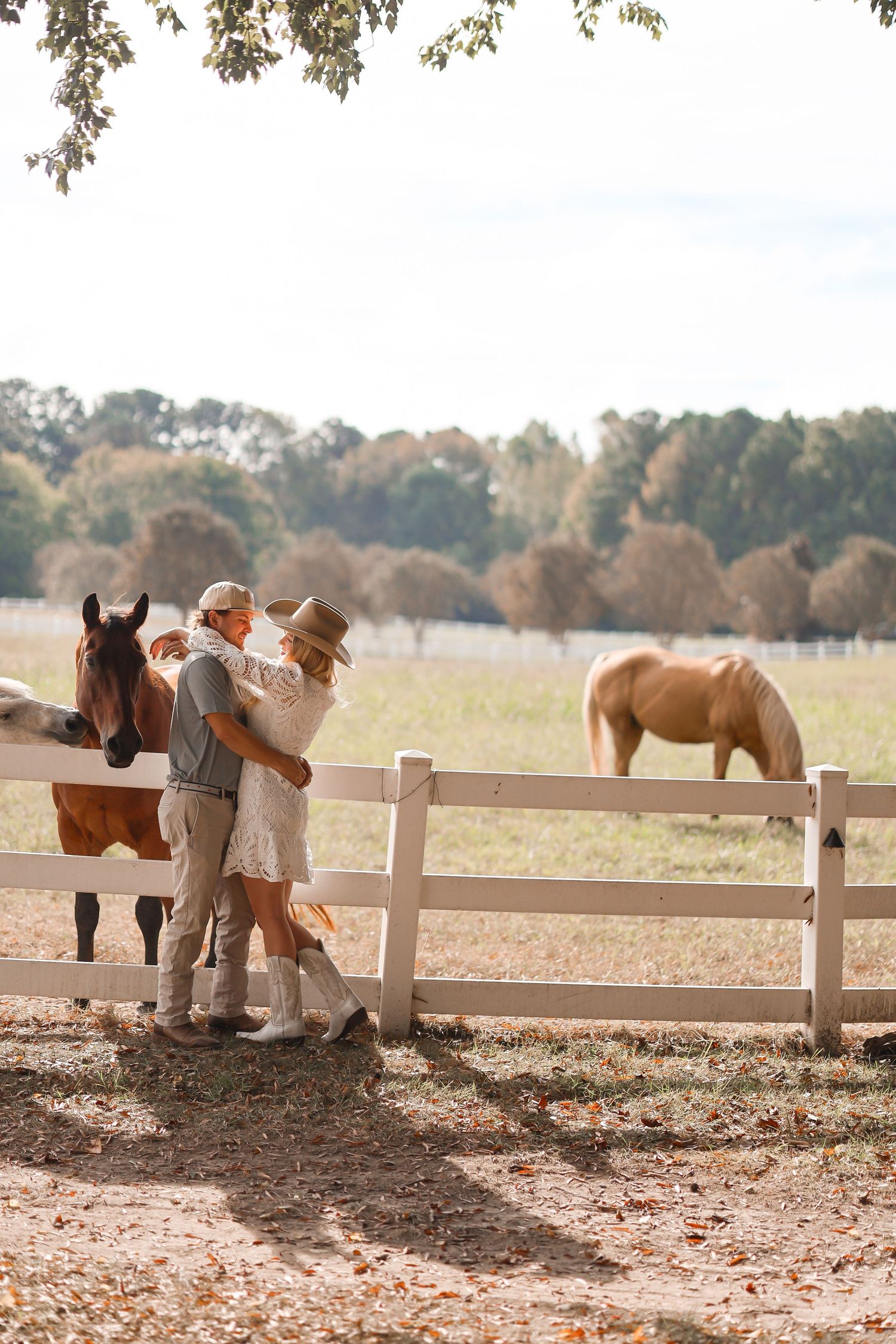 a couple posed in front of a field of horses roaming, engagement photography in raleigh