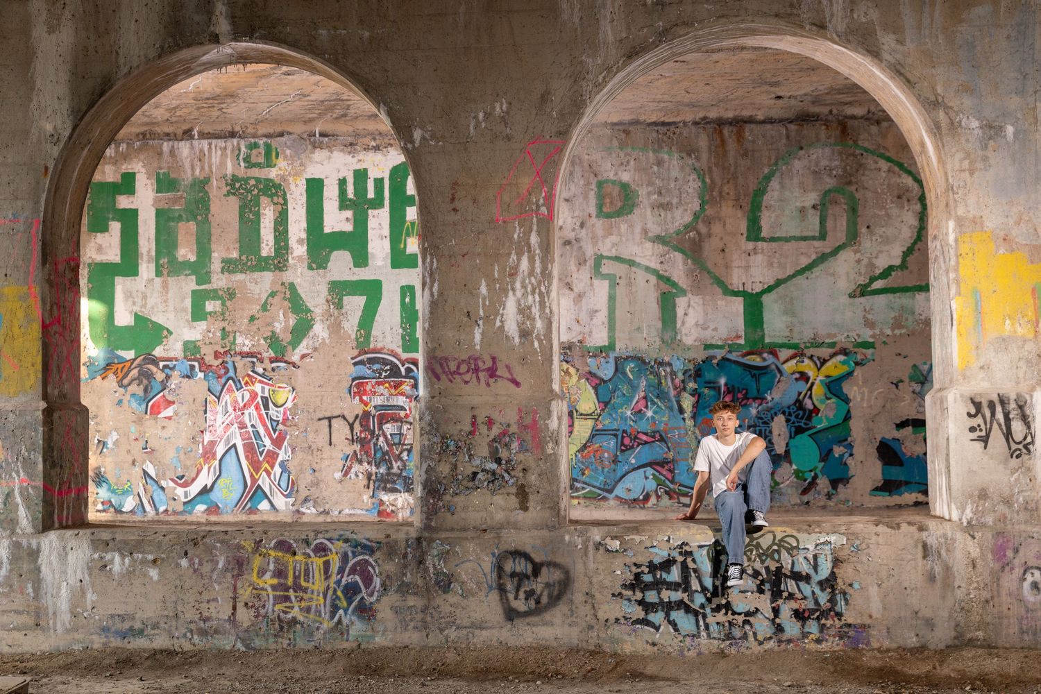 Person standing beneath graffiti-covered concrete arches in an urban underpass with colorful street art.