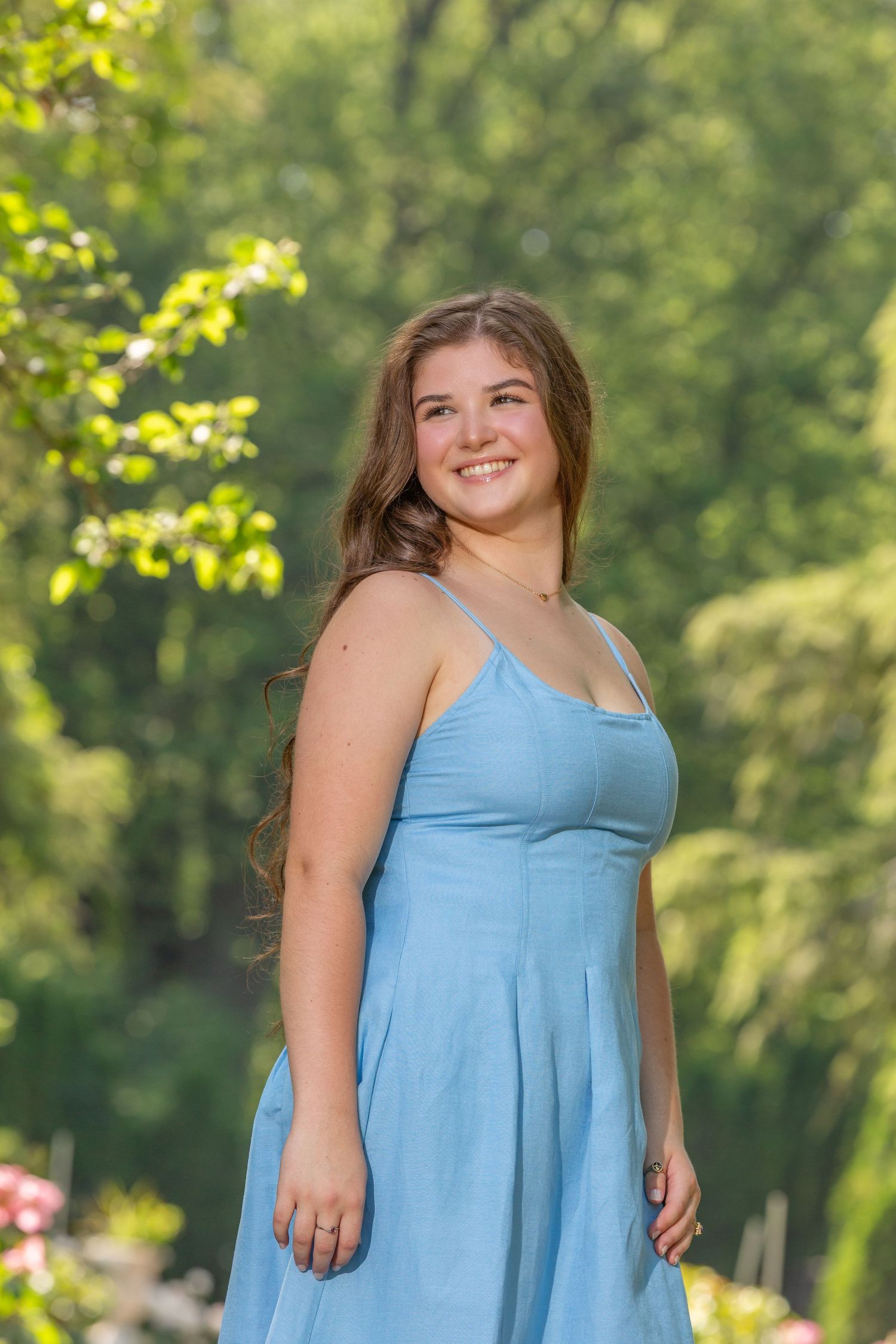 A person wearing a light blue sleeveless summer dress poses outdoors against a green natural background.