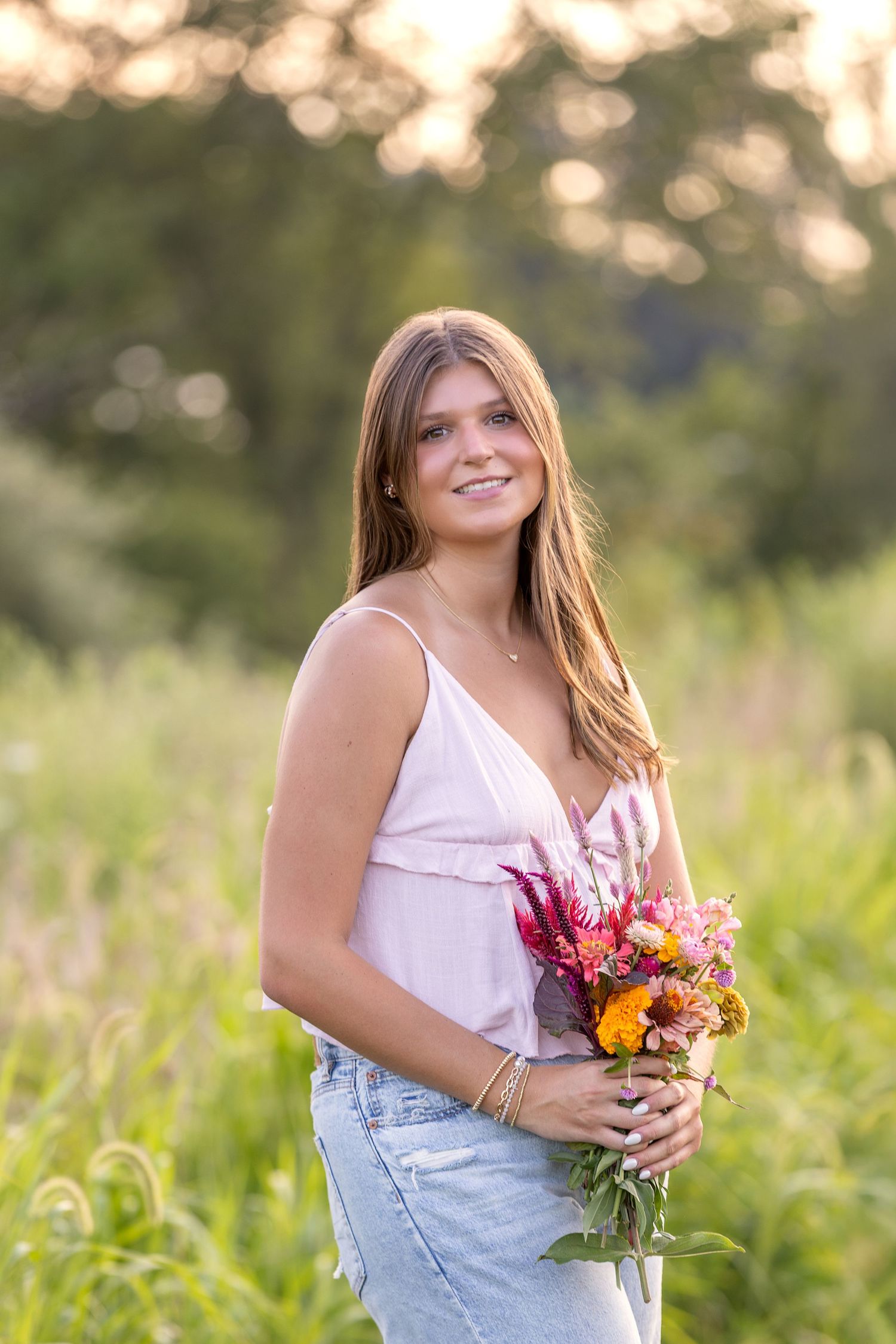 Smiling teenage girl holding a vibrant bouquet of wildflowers in a sunlit green meadow.