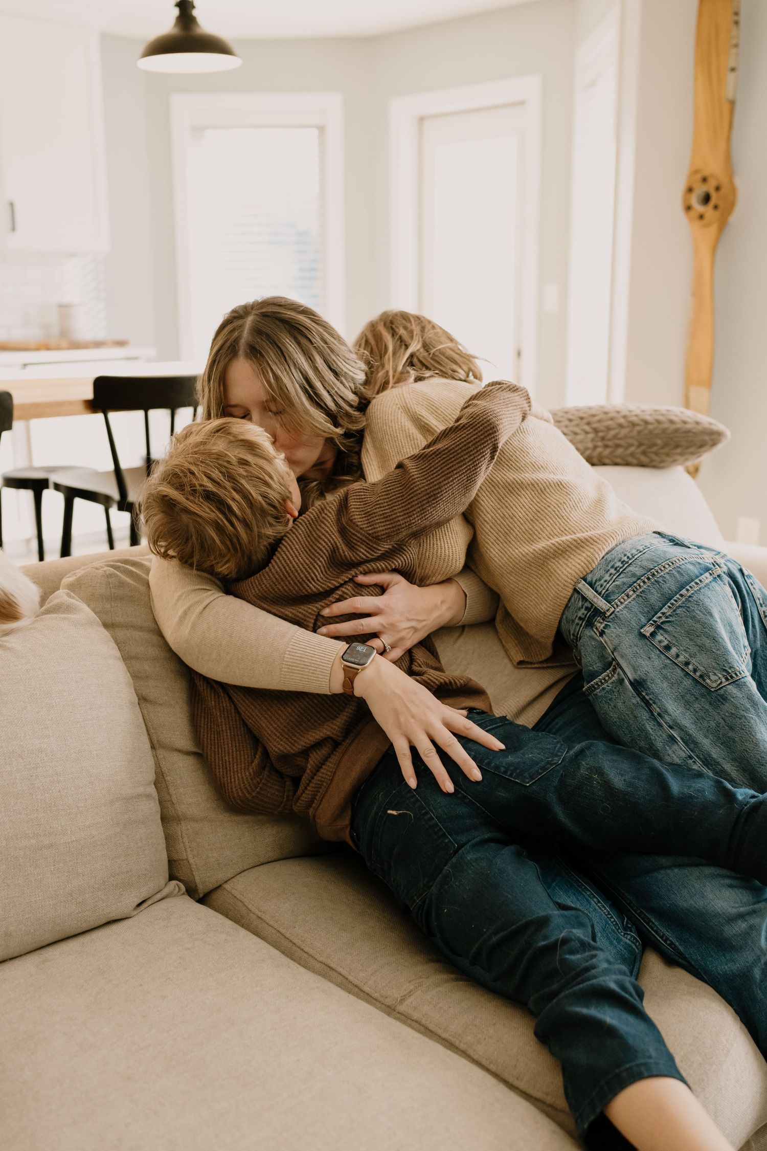 A tender family moment shared on a beige couch in a bright, minimalist living room.