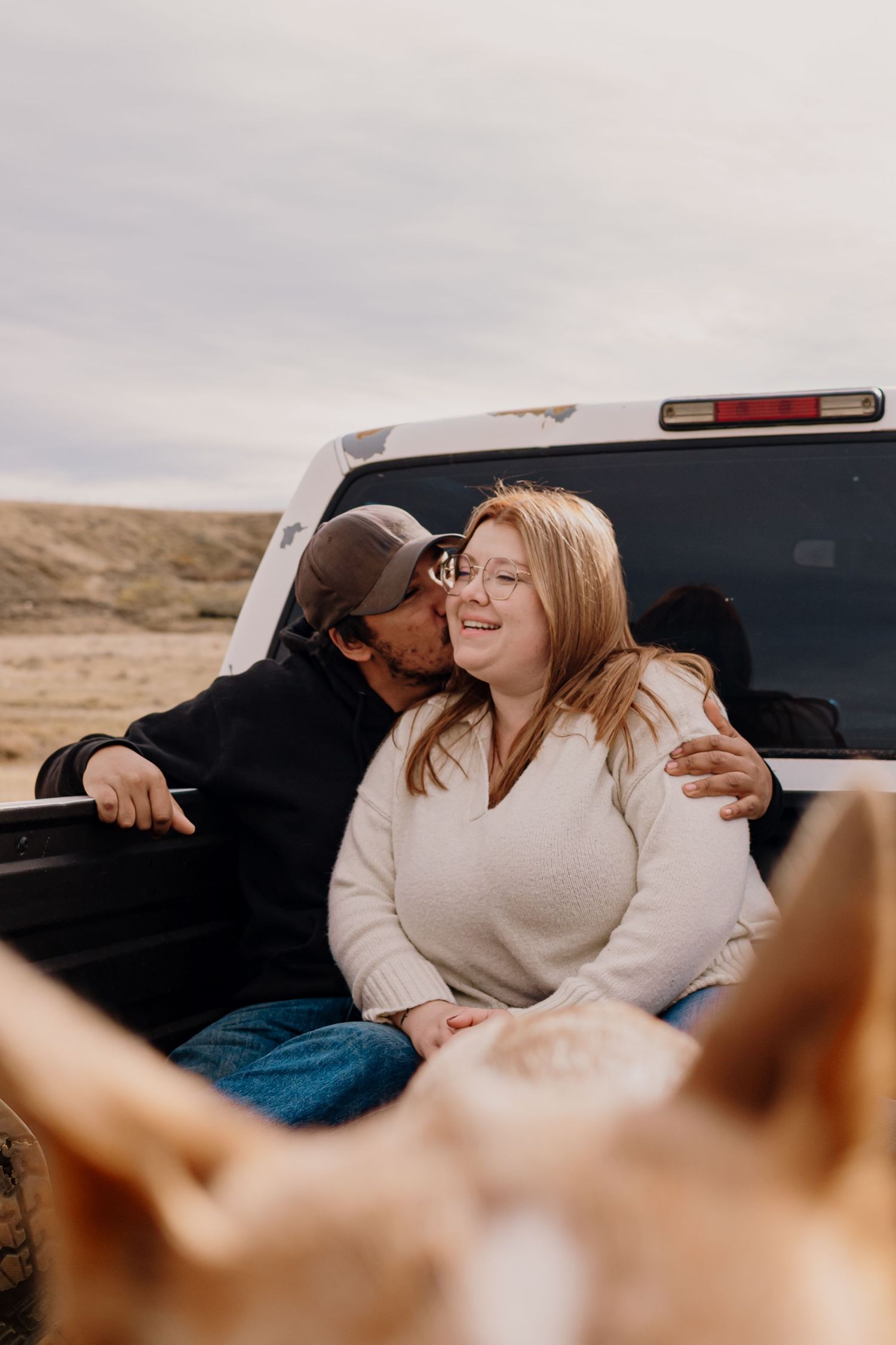 A couple shares laughter while relaxing in the back of a vehicle in a desert setting.