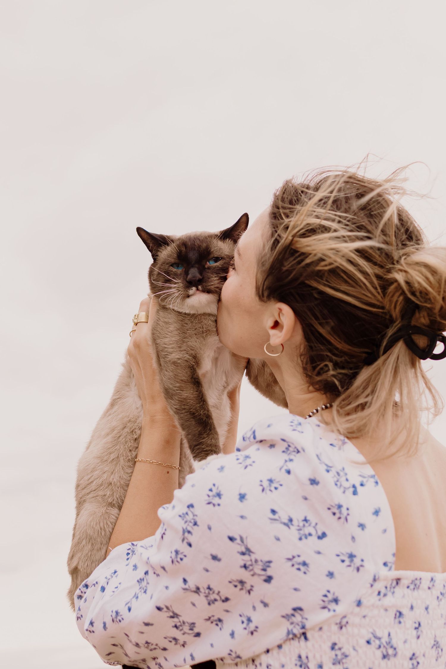 A person in a floral print shirt holds and kisses a gray cat in a series of affectionate poses against a white background.