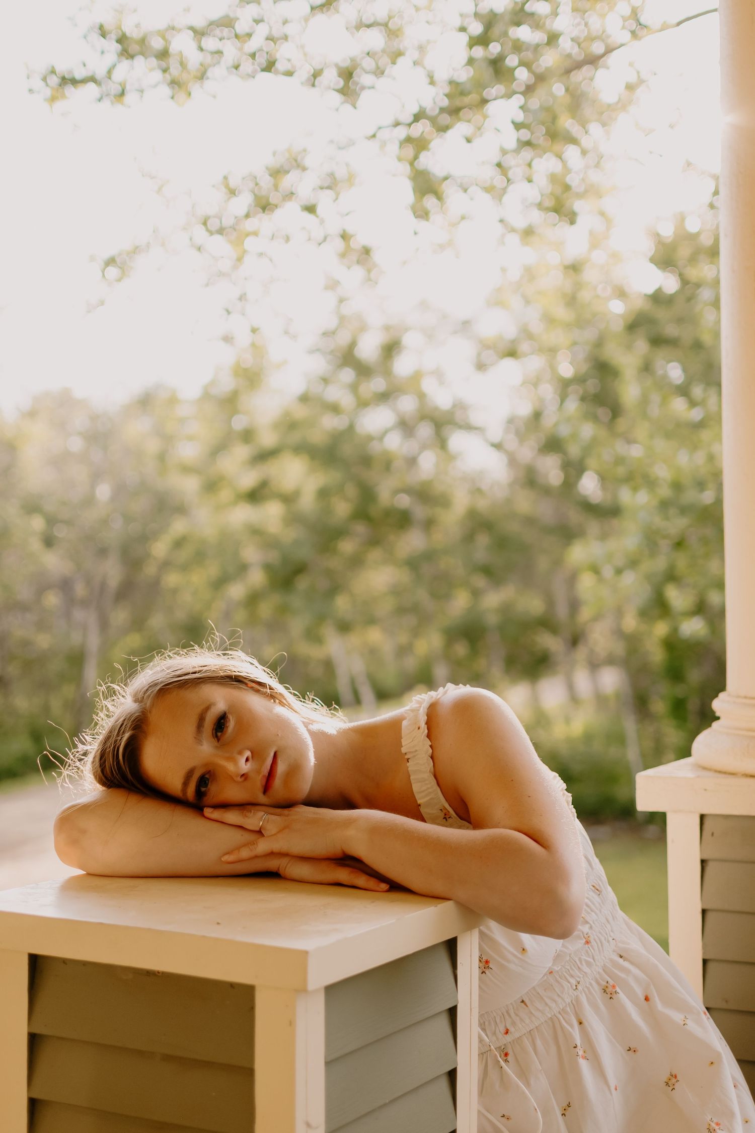 A dreamy summer portrait in soft golden light shows someone resting on a white wooden surface outdoors.