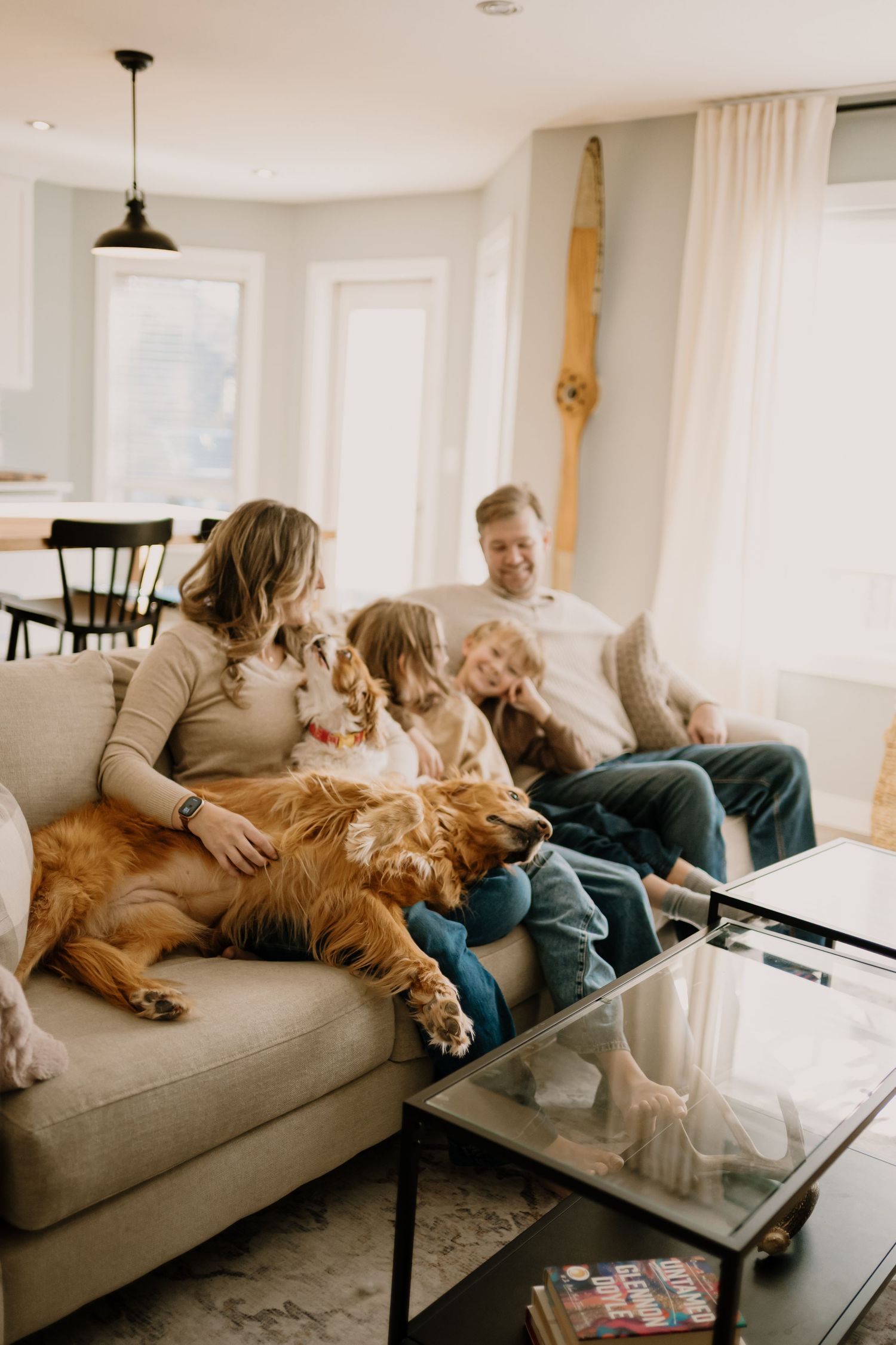 A sequence of four photos showing people relaxing on a couch with a golden retriever dog at home.