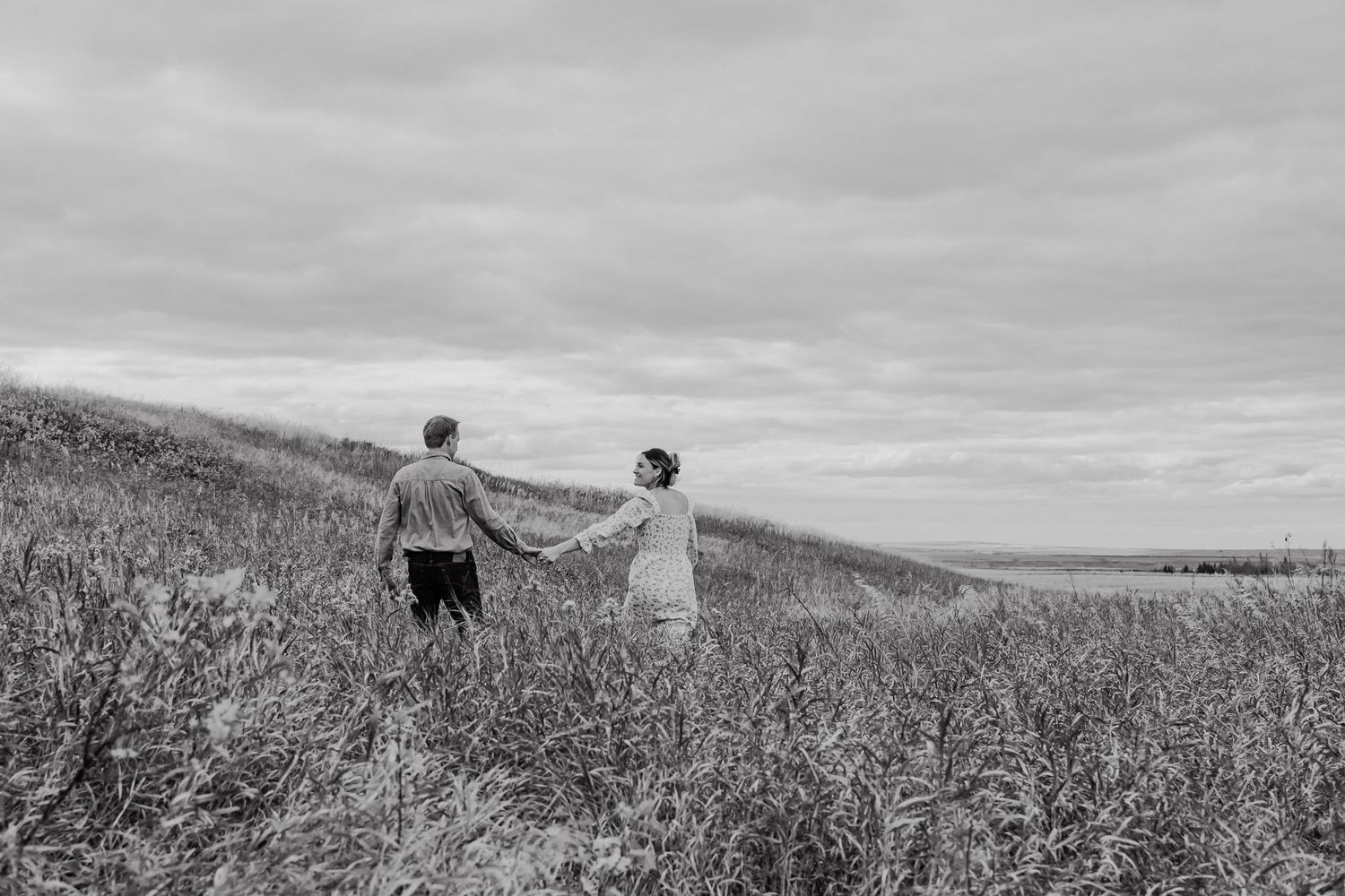 Black and white panoramic photo series showing a couple walking through a scenic meadow with blanket and picnic basket.