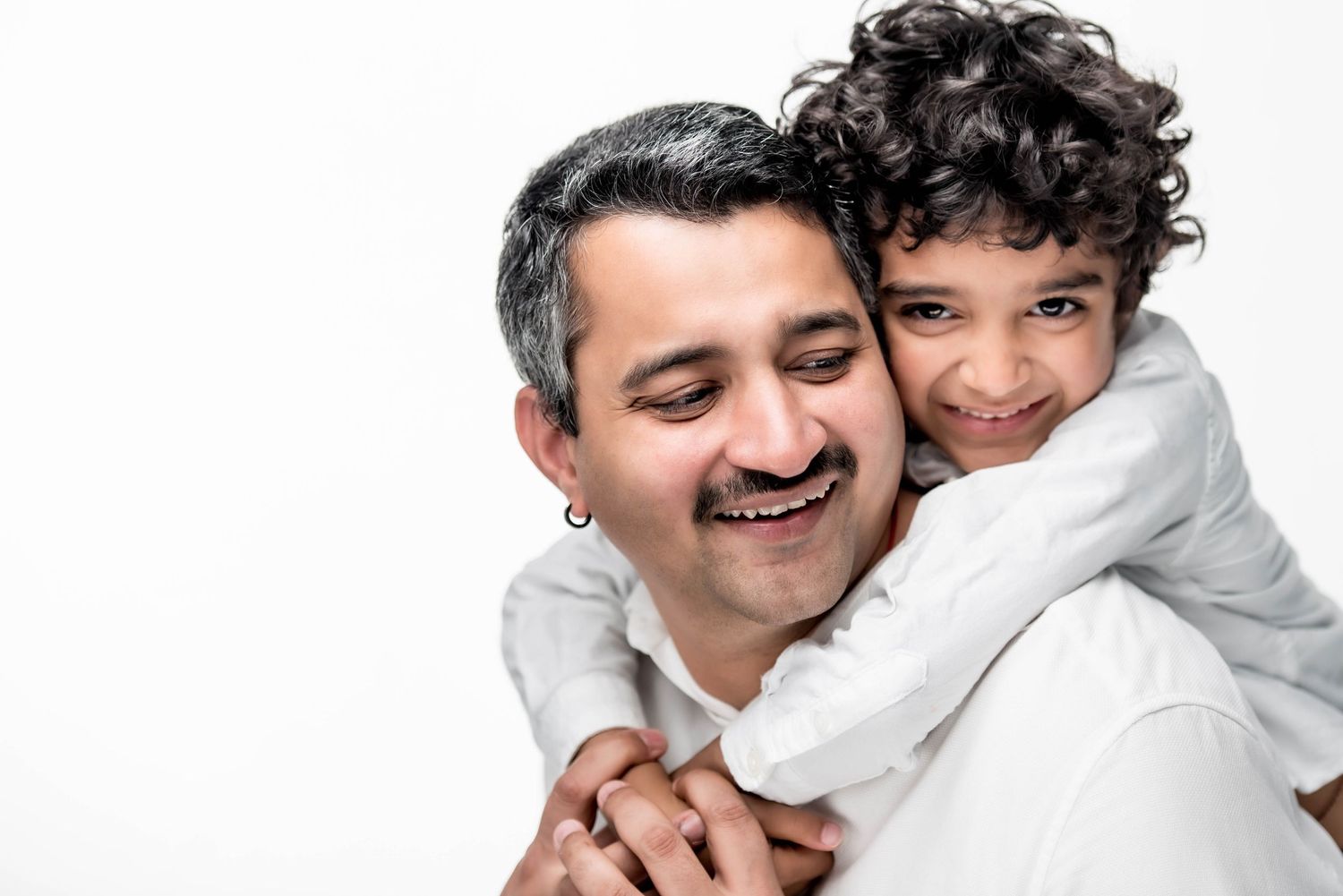 A joyful father and child share a warm hug, smiling together against a white background.