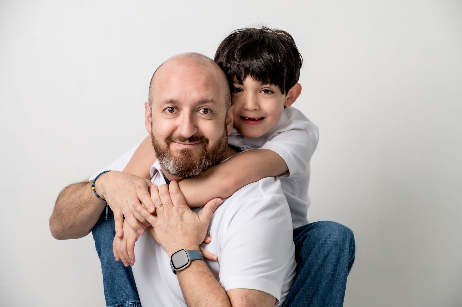 “father and son portrait smiling child hugging dad white background family photography studio candid moment”