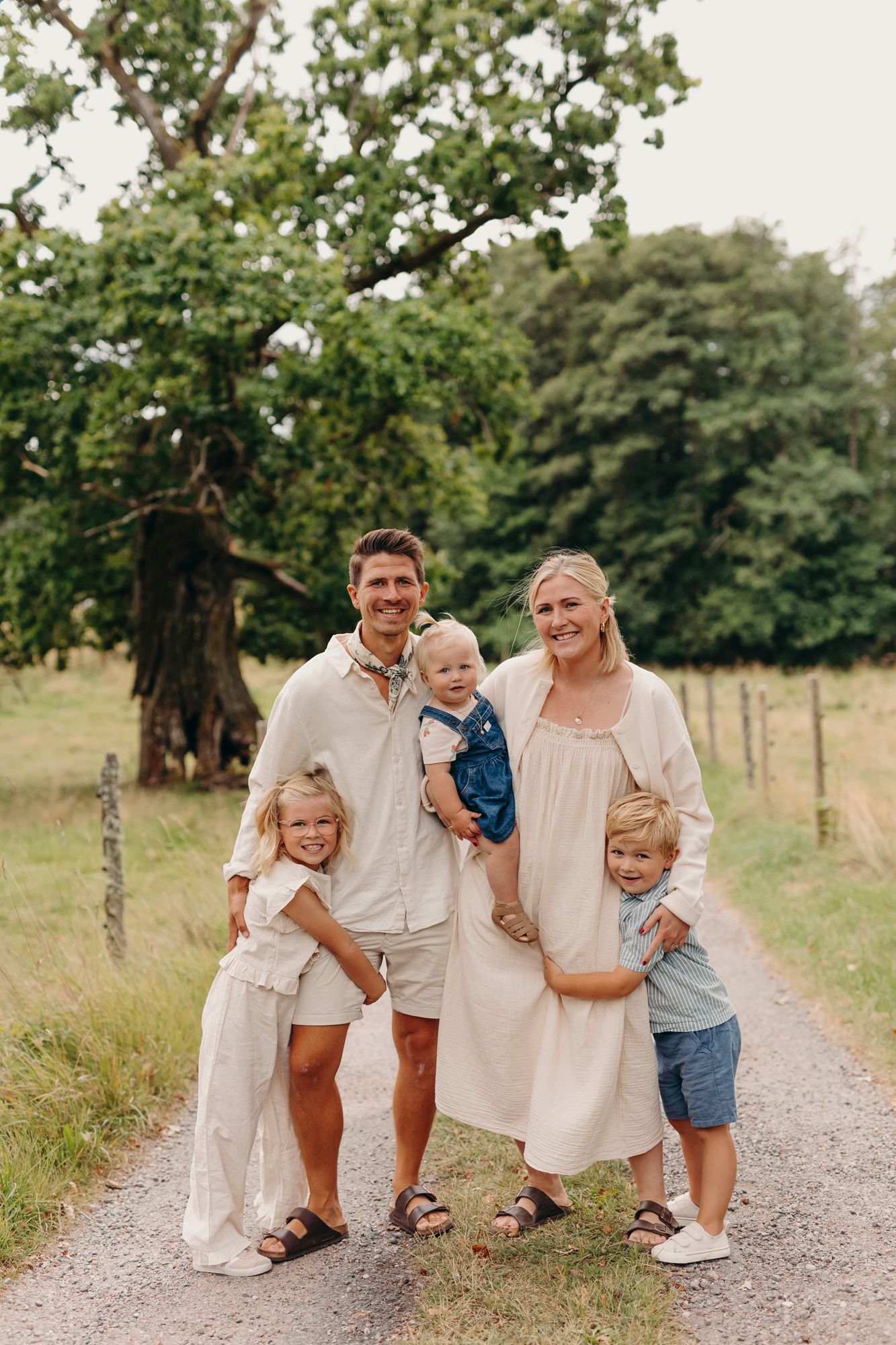 A family standing together on a gravel path in a rural setting with green trees and grass in the background.
