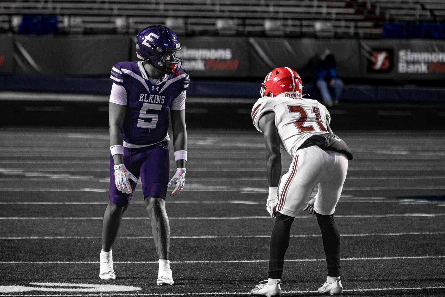 Football players in purple and red uniforms face off on a football field during a competitive match.