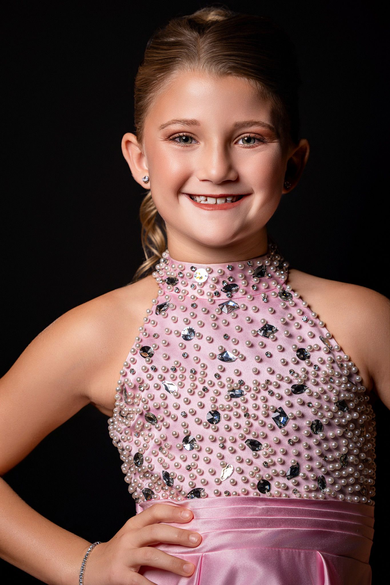 Young girl in pink beaded halter dress smiling confidently against dark background.