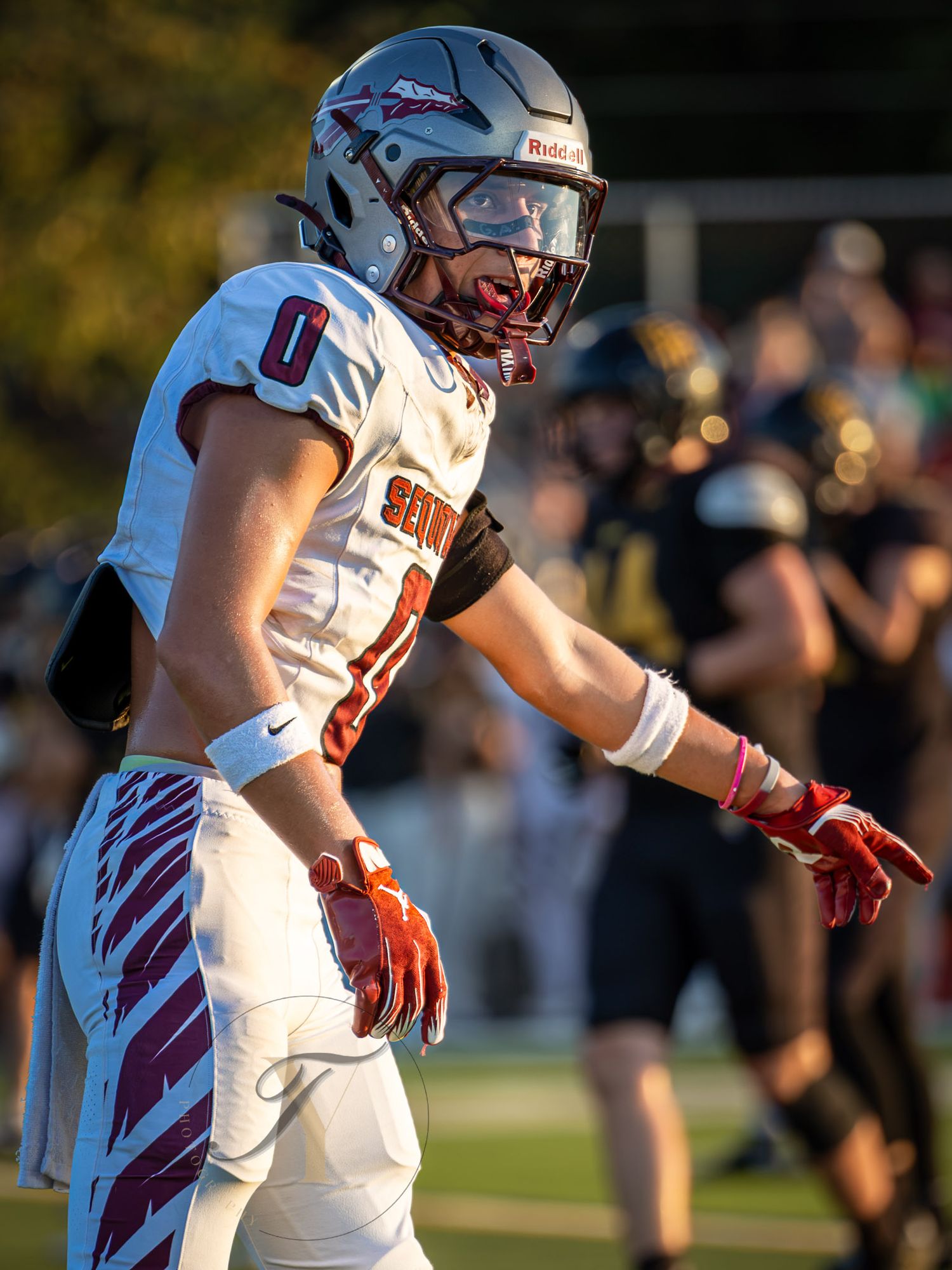 Football player wearing number 0 in white and red uniform poses on field during a game under warm evening light.