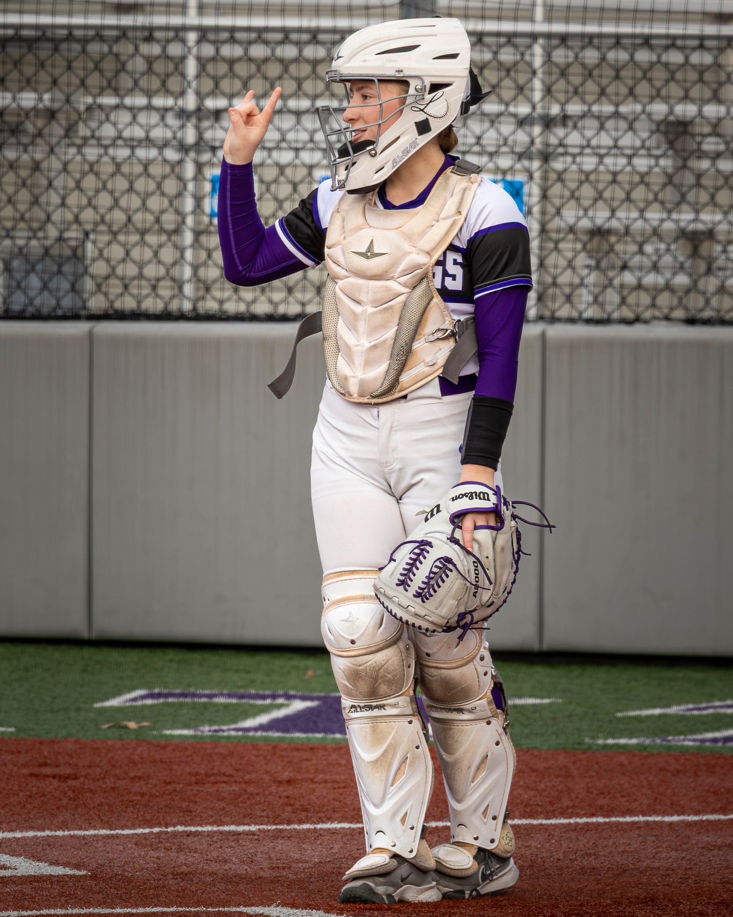Baseball catcher in white uniform and protective gear crouches in ready position behind home plate during game.