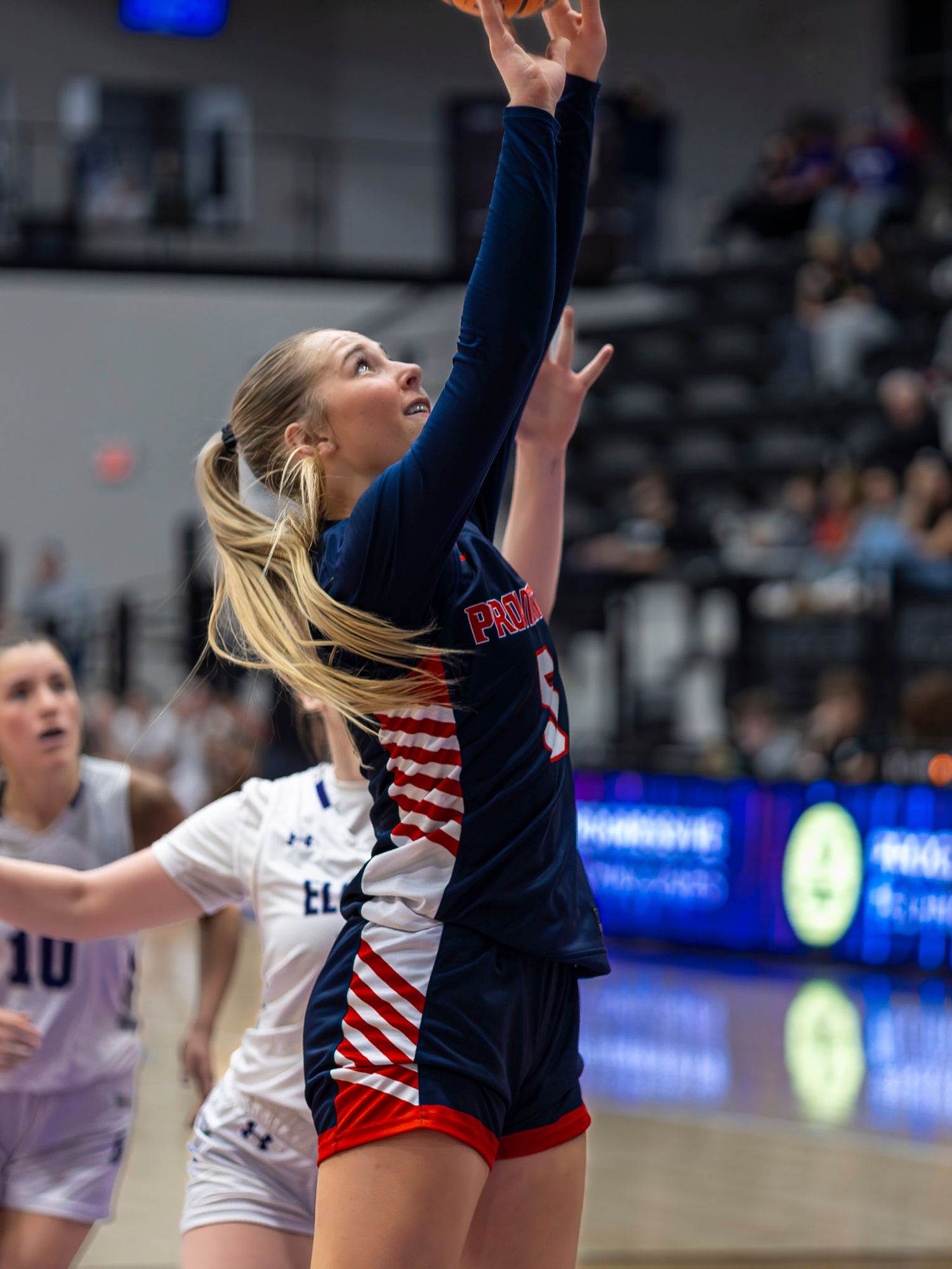Volleyball players leap high to block a shot at the net during an intense indoor match.