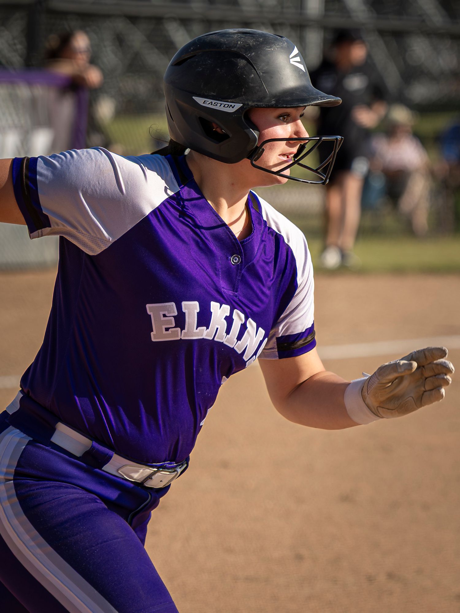 Elkins softball player in purple uniform and black helmet runs the bases during a competitive game.