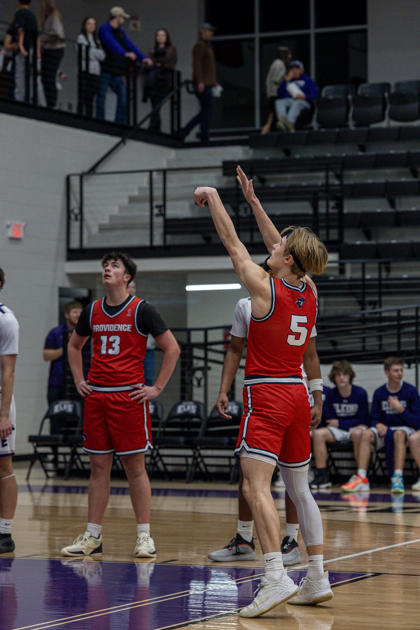 Volleyball players in red uniforms dive and stretch for the ball during an intense match sequence.