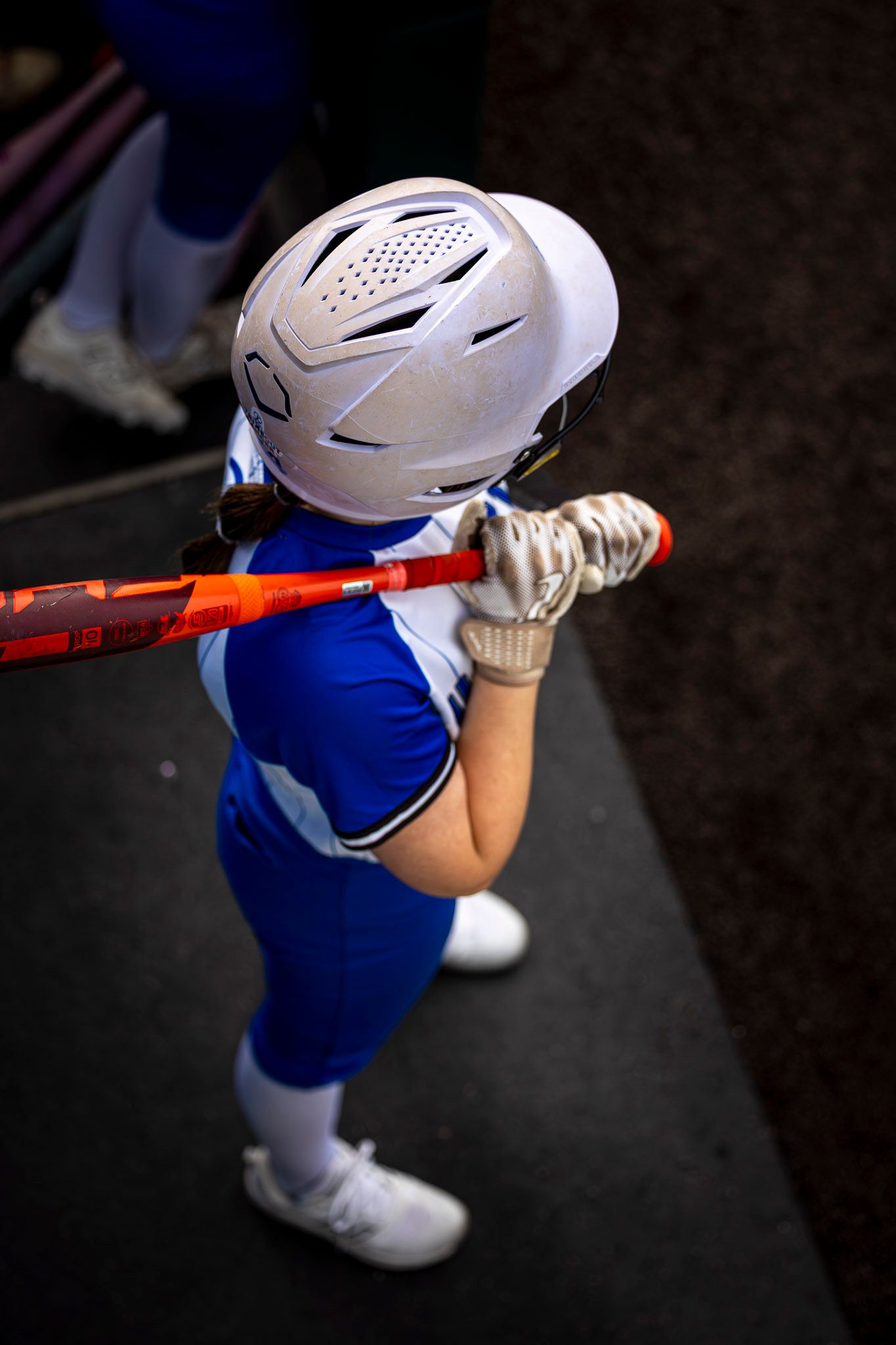 Young softball player in blue uniform and white helmet holds orange bat in batting stance.