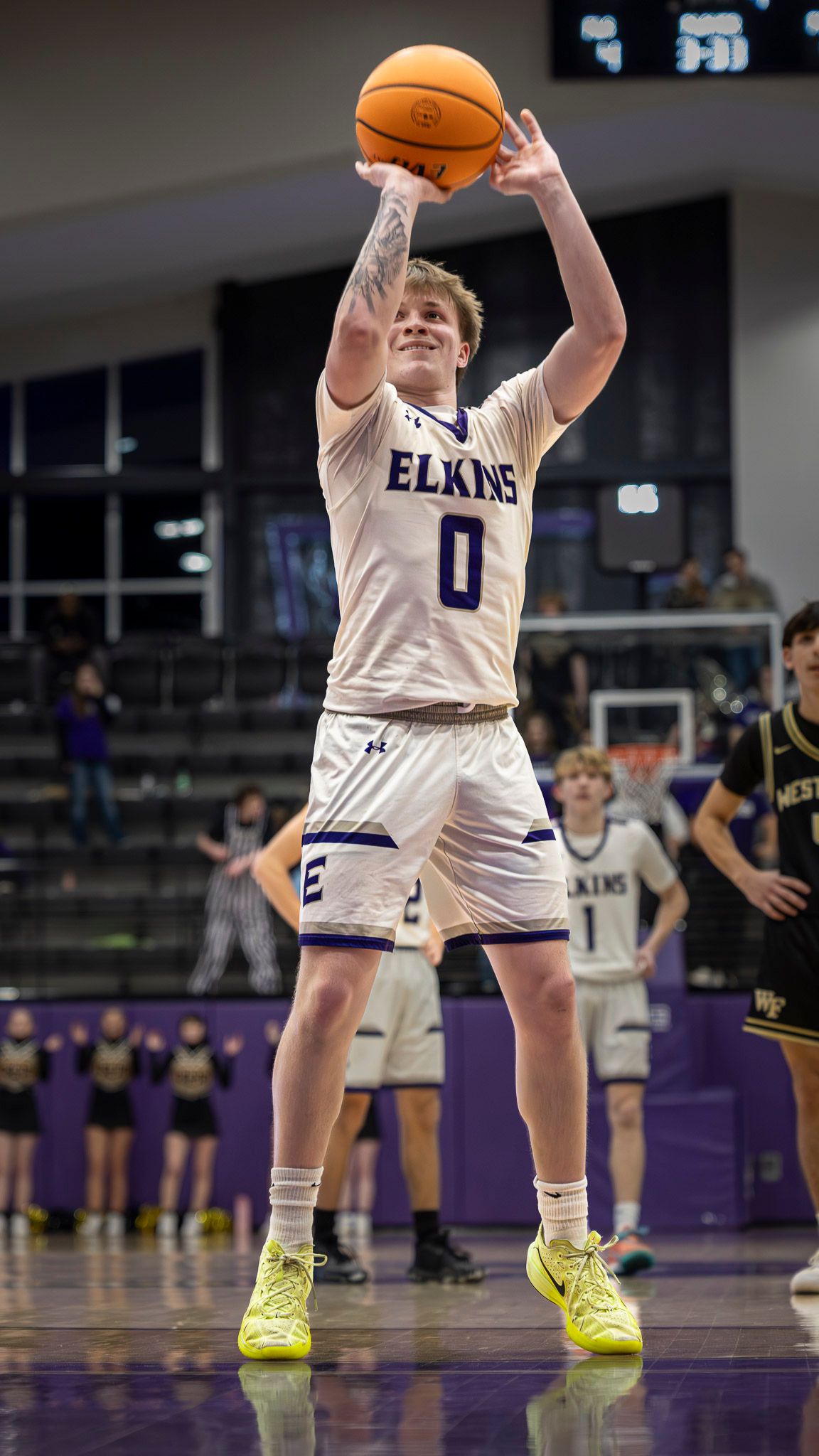 Basketball player in white Elkins jersey number 0 takes a jump shot during game on purple court.