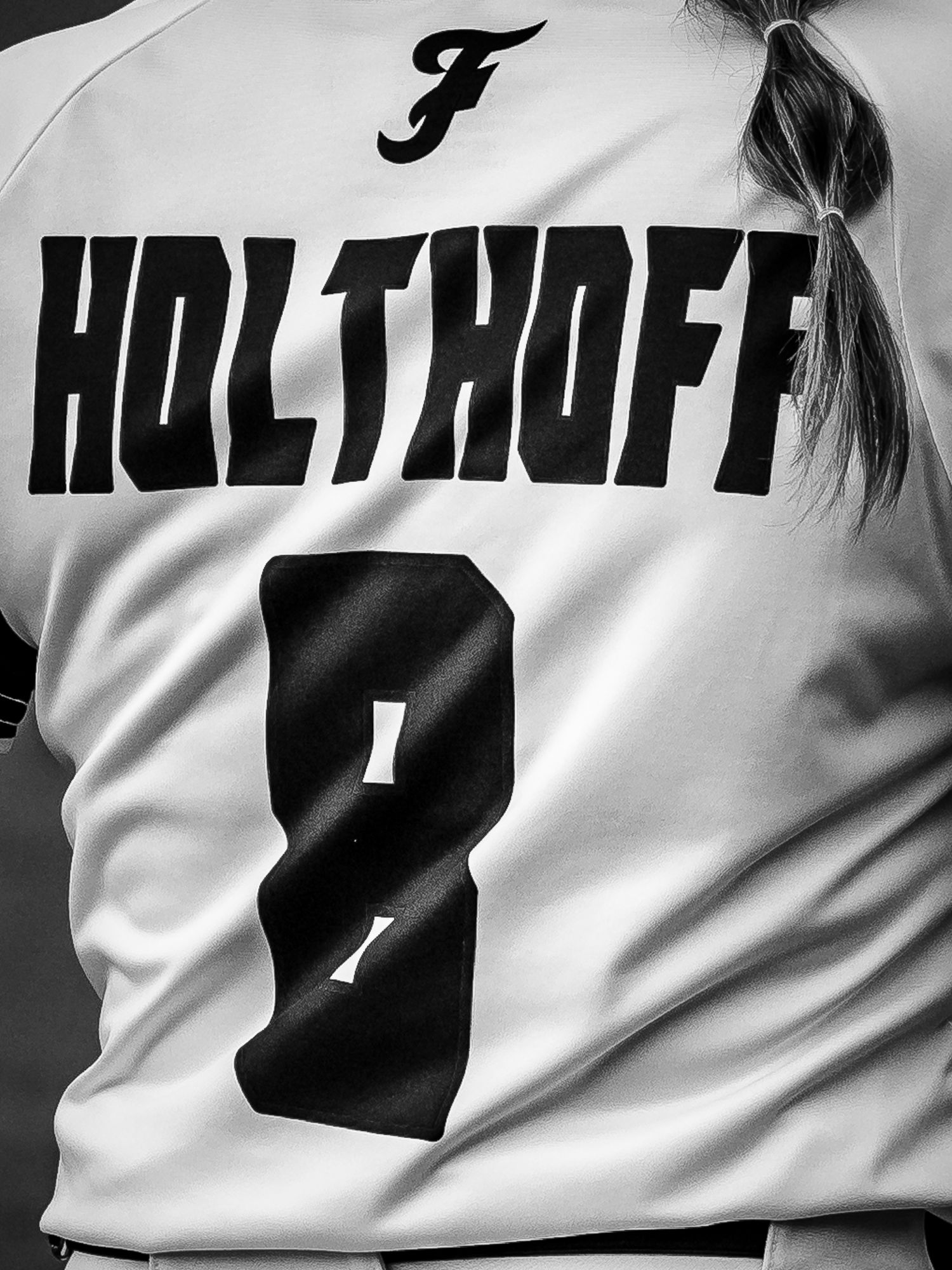 Black and white rear view of a softball player in a number 8 Holthoff jersey with a ponytail and a script F logo on the collar.