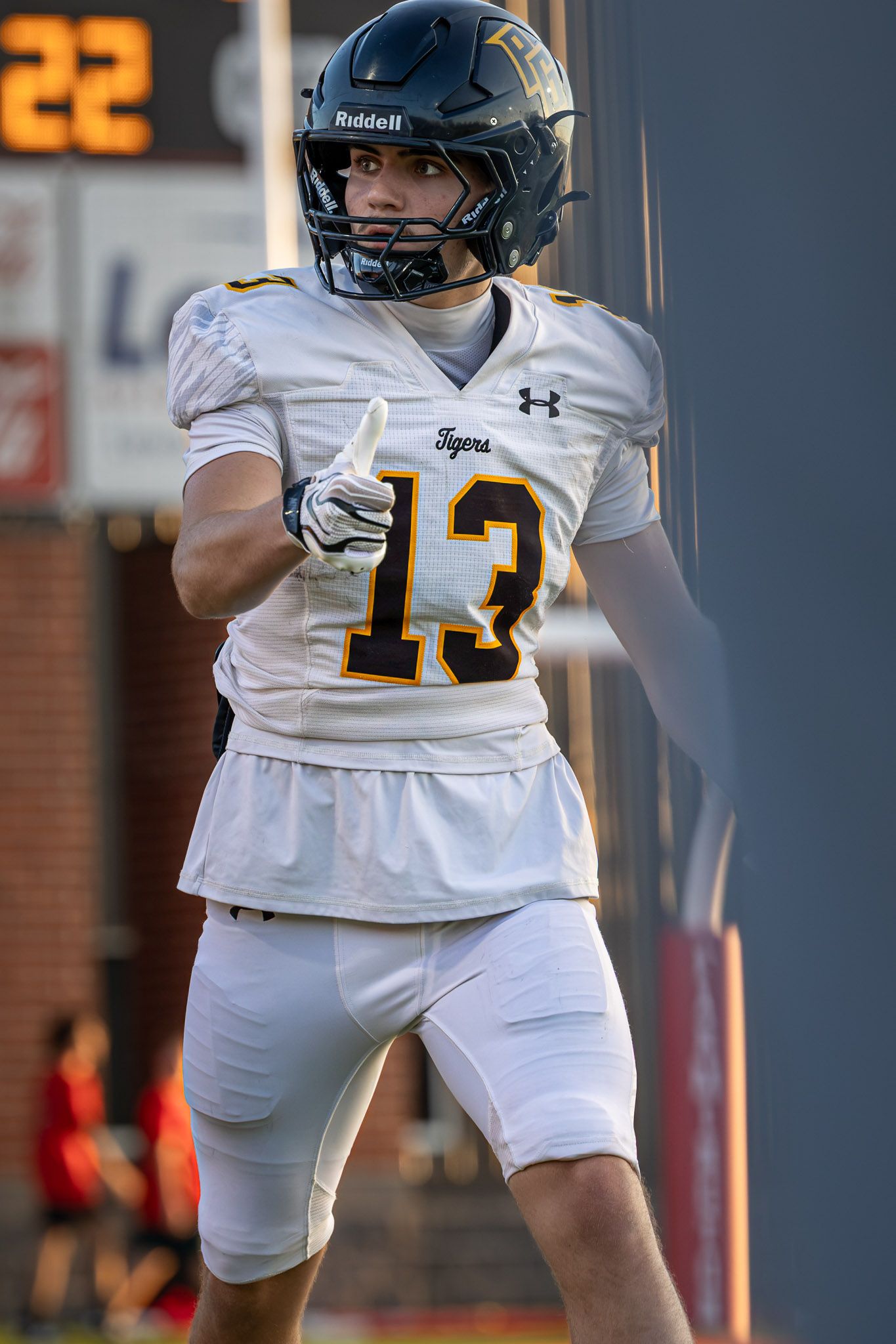 Tigers football player in white number 13 jersey and black Riddell helmet gives a thumbs up on the field during a game.