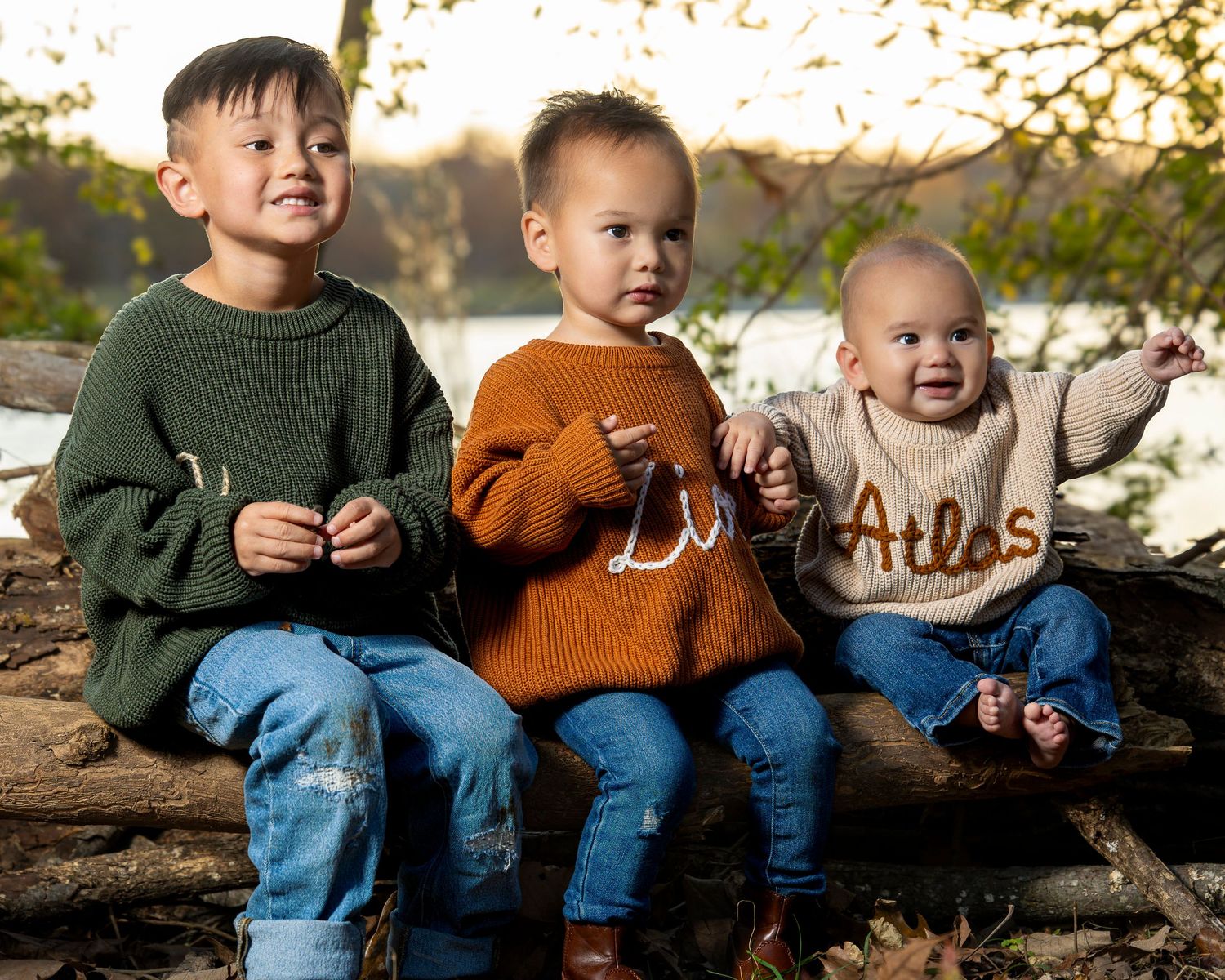 Children in casual fall outfits sit together on a log outdoors while laughing and playing in autumn sunlight.