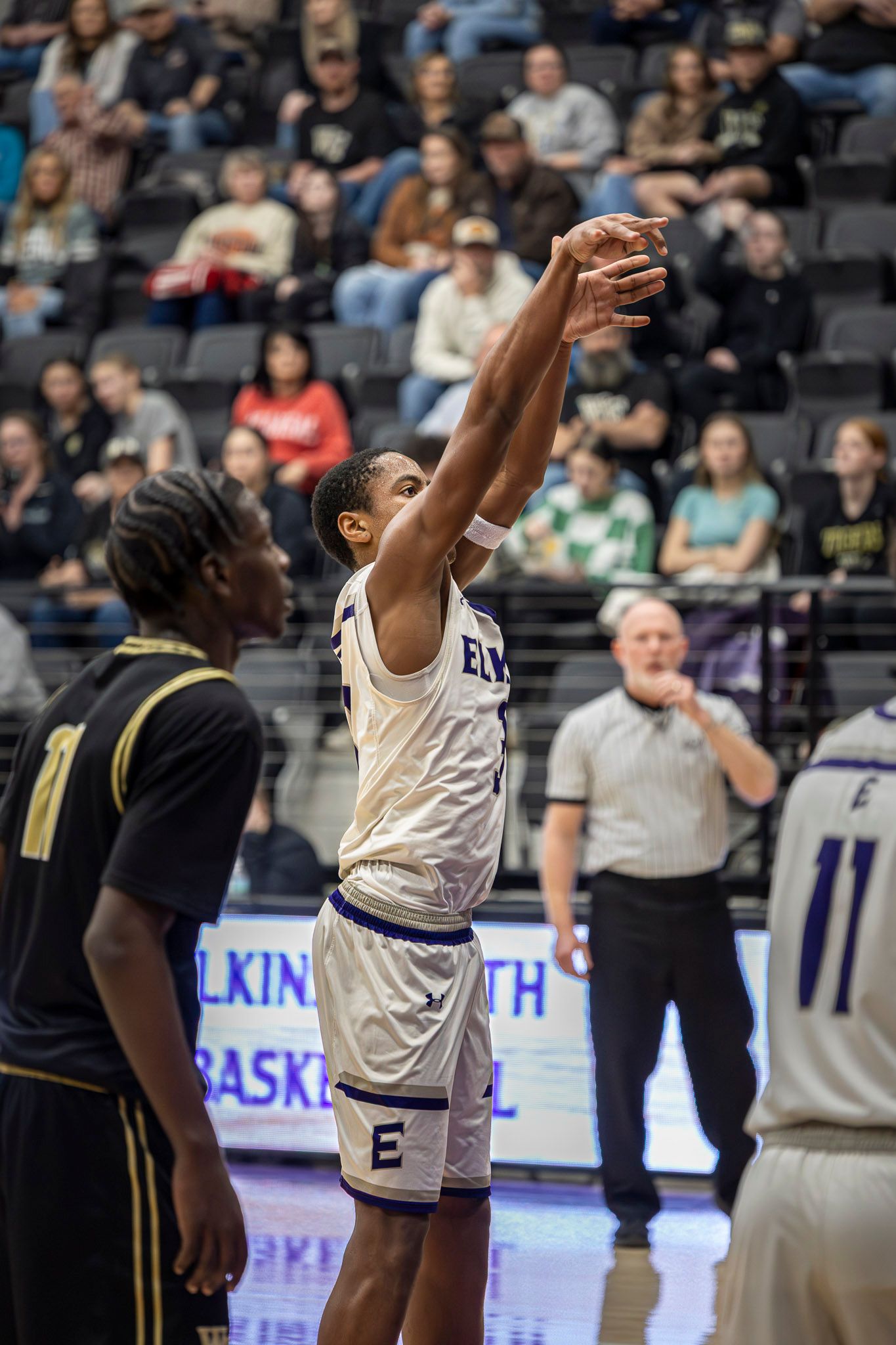 Basketball players compete for a rebound during an intense game in a crowded indoor arena.
