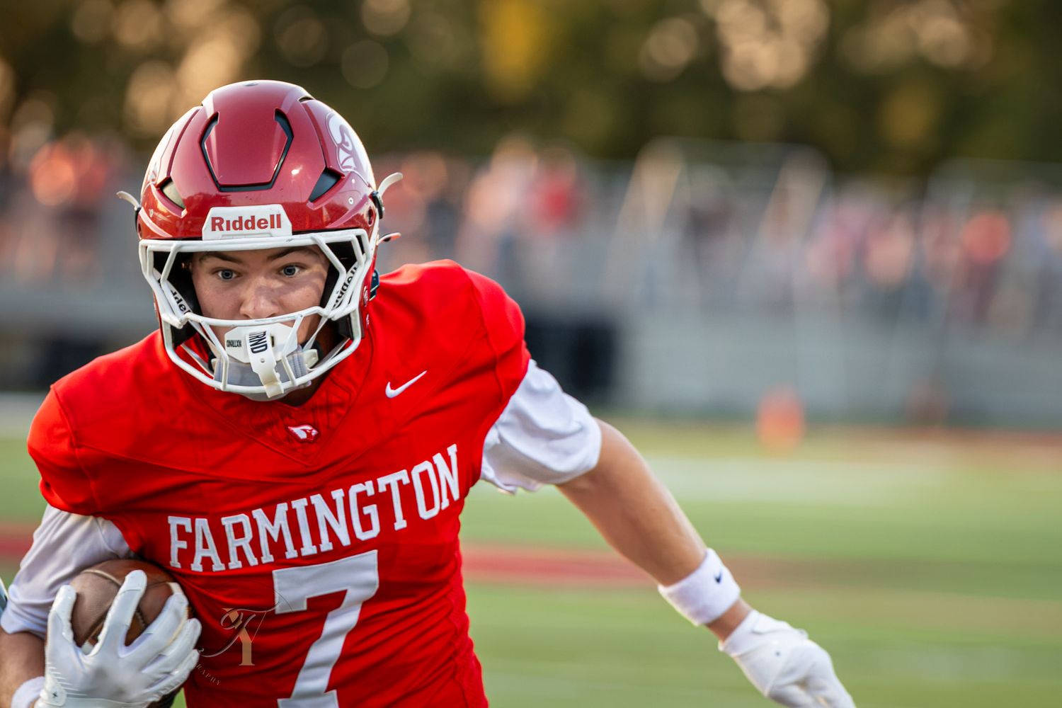 Farmington football player #7 in red uniform runs with ball during a game wearing Riddell helmet.
