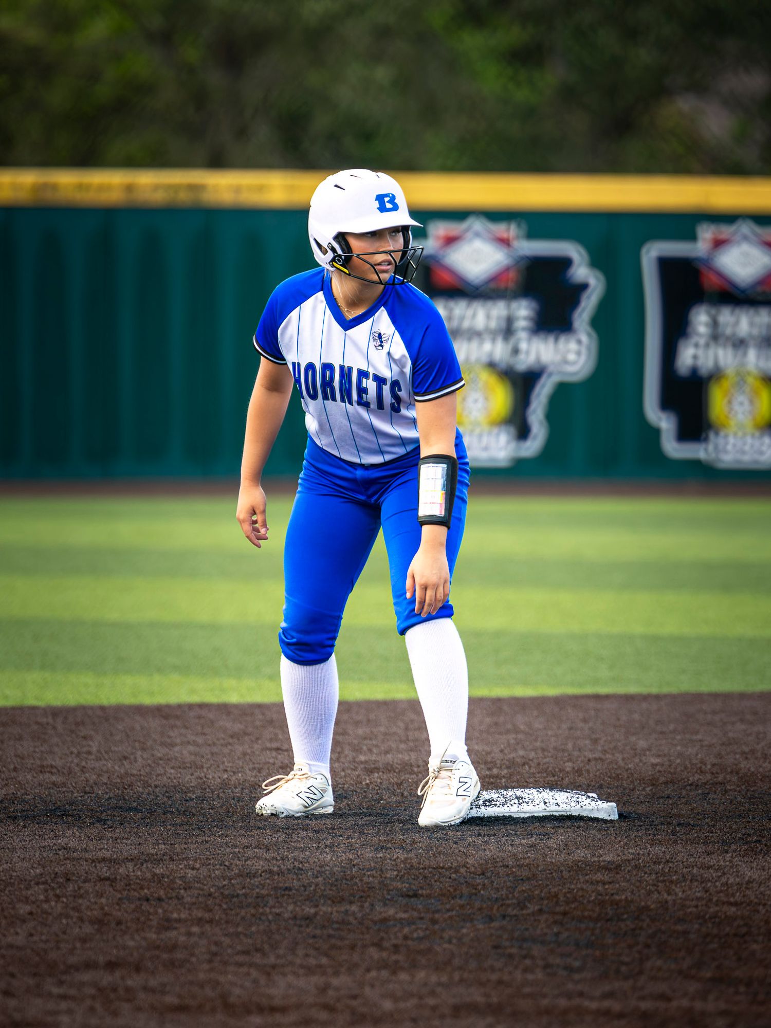 Hornets softball player in a blue uniform and white batting helmet stands on second base with a ready stance on the field.