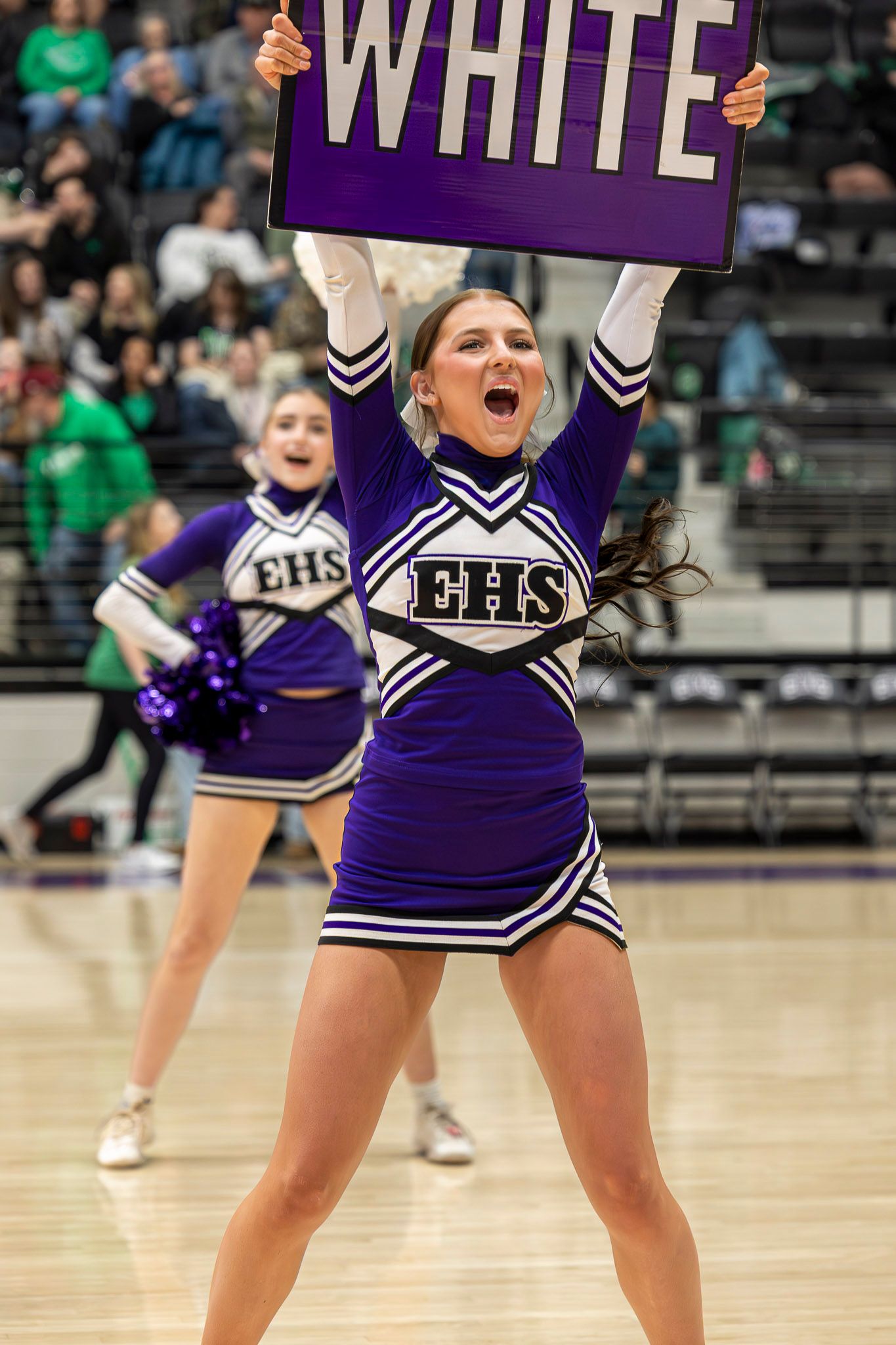 Cheerleaders in purple and white uniforms perform a synchronized dance routine on a gymnasium floor.