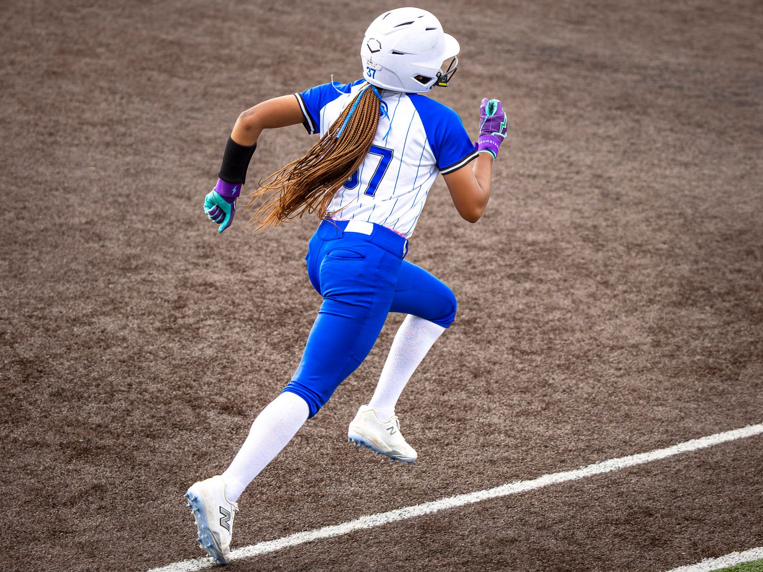 Female softball player in blue uniform sprinting on the field during a game.