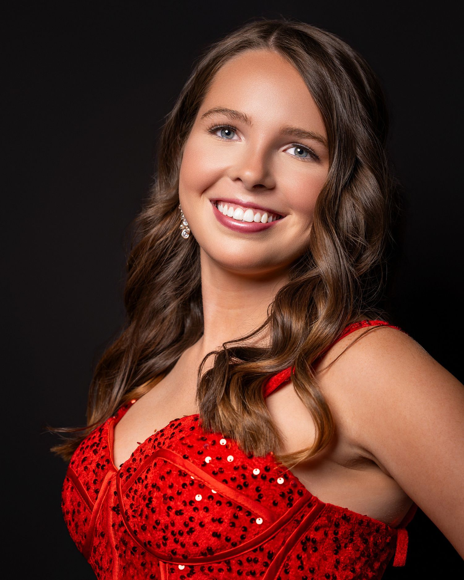 Young woman smiling in a red sequined dress against a dark background, professional portrait photography.