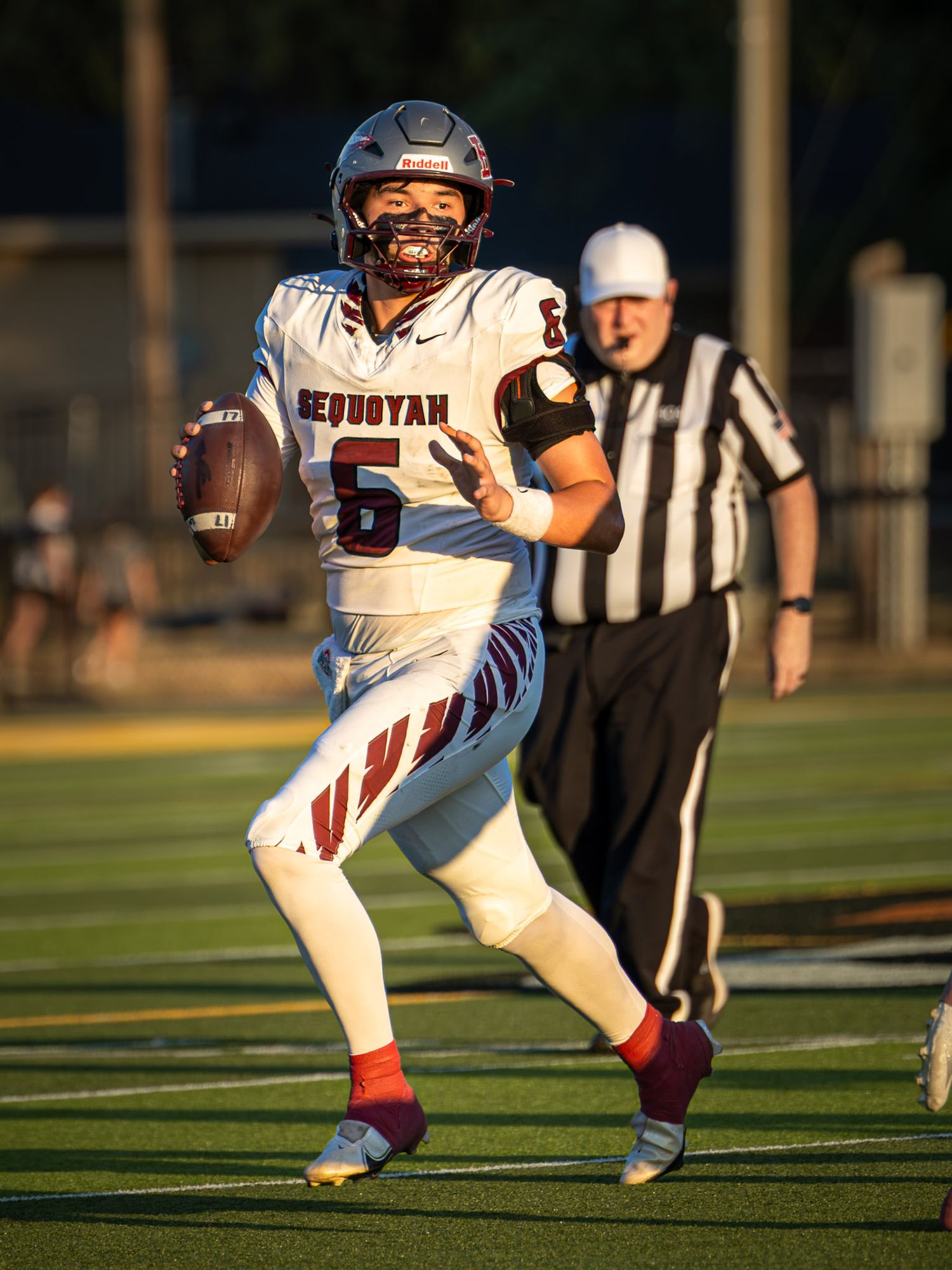 Sequoyah high school football quarterback wearing number 5 looks downfield with the ball while a referee watches in the background.