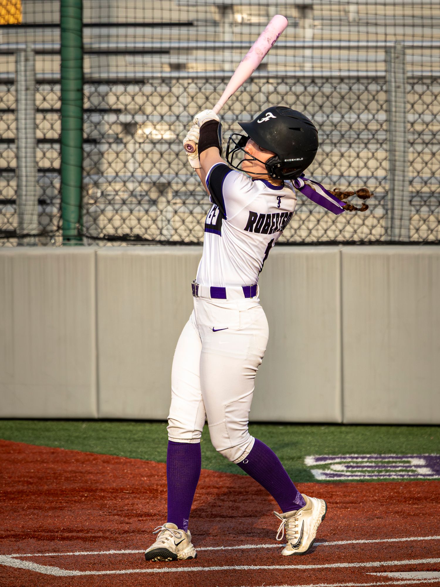A softball batter follows through on their swing at home plate during a competitive game.