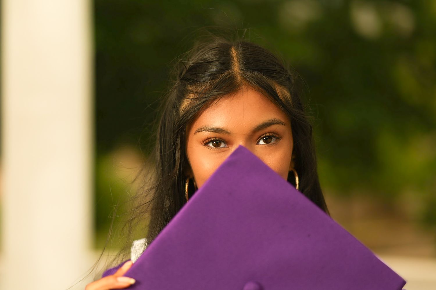 A young woman with long dark hair is holding a purple cloth in front of her face, partially obscuring her features.
