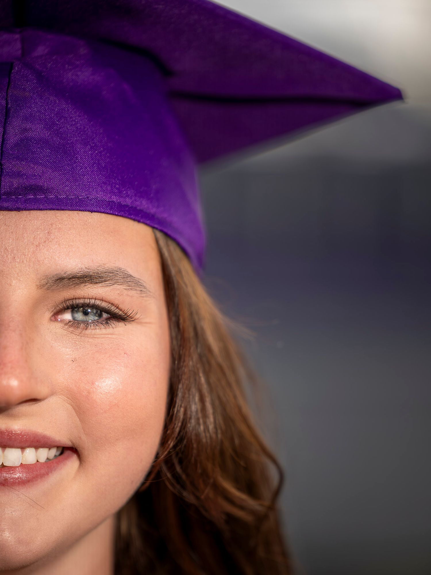 Smiling young woman wearing a purple graduation cap, close-up portrait photo of a graduate.