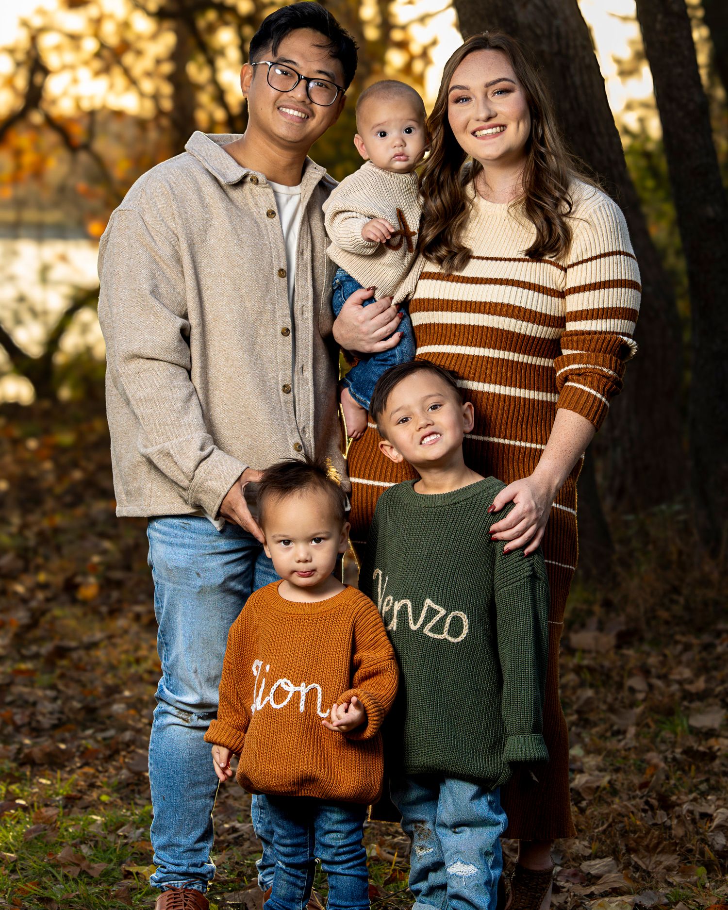 A family wearing coordinating fall outfits poses together in a wooded setting during autumn.