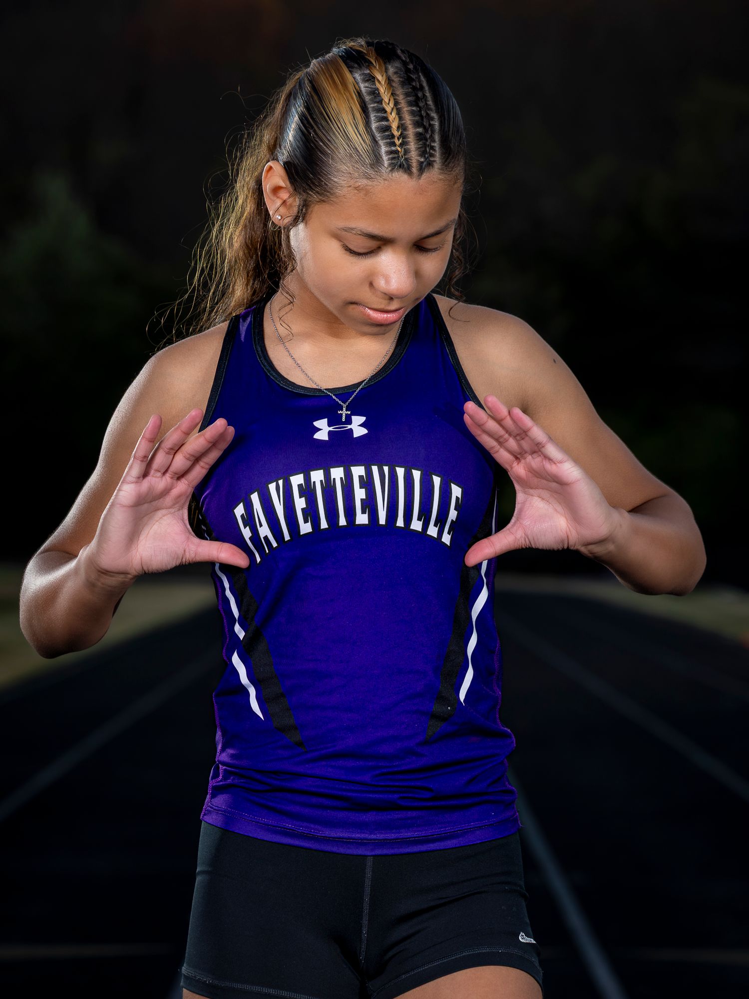 Young female athlete in purple Fayetteville track jersey poses on running track, hands extended forward.