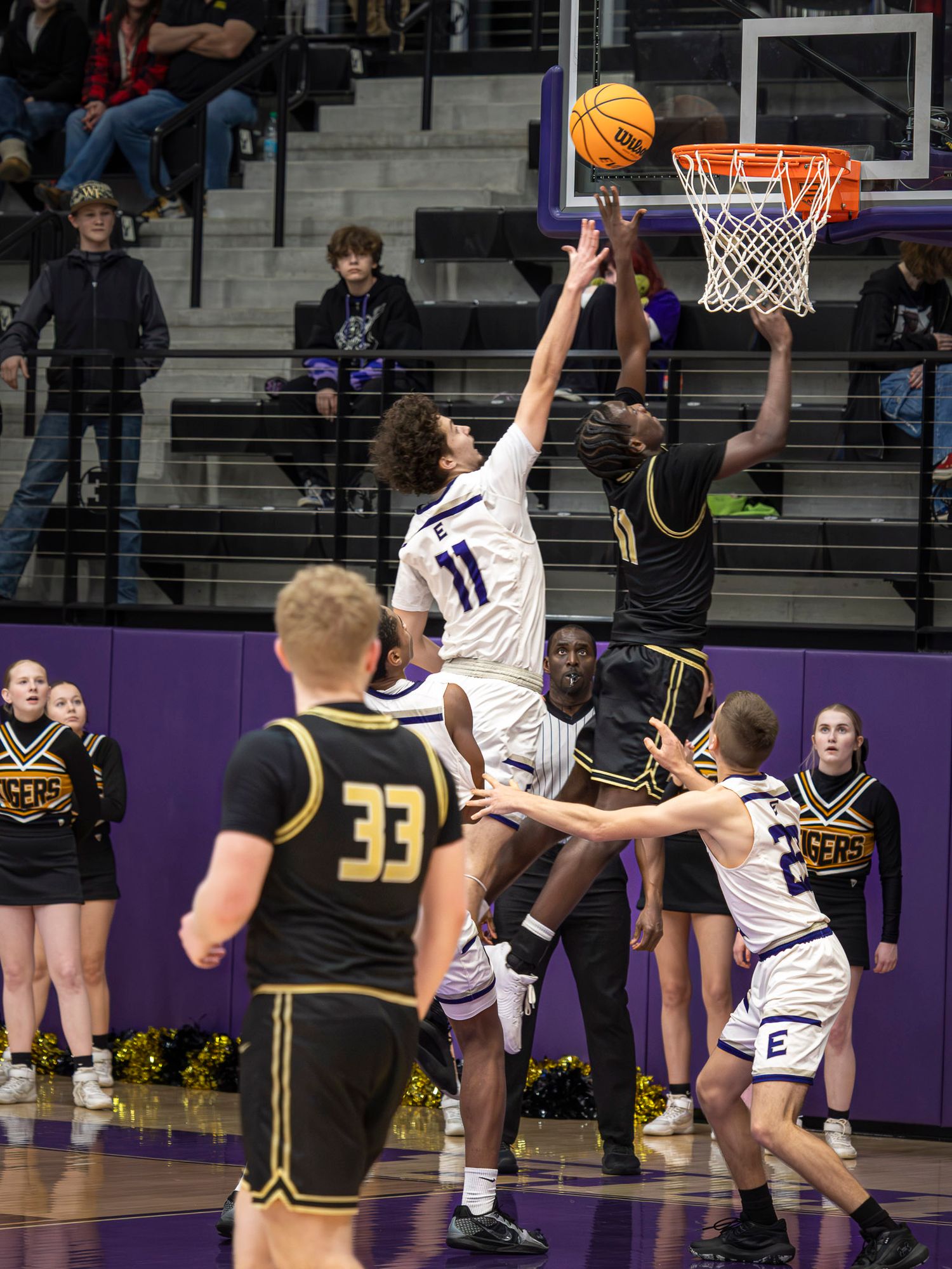 Basketball player in white jersey leaps high for a layup against defenders in black uniforms during an intense game.
